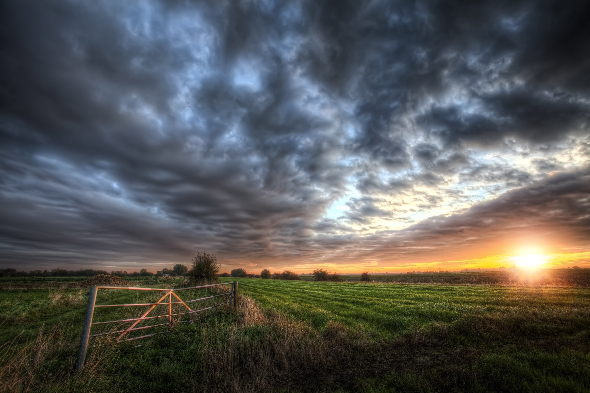 Sunset over a green field with a gate HD Wallpaper