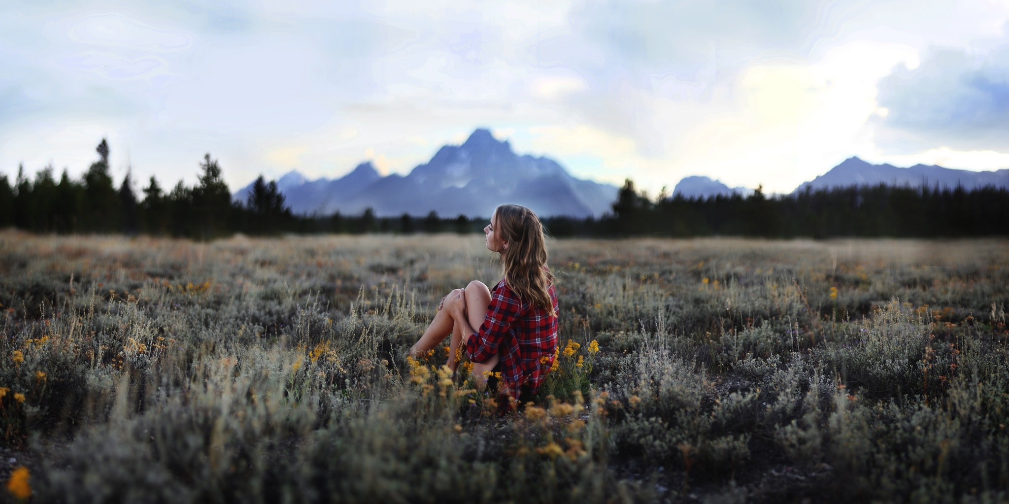 Woman sitting in a field with mountains in the background HD Wallpaper