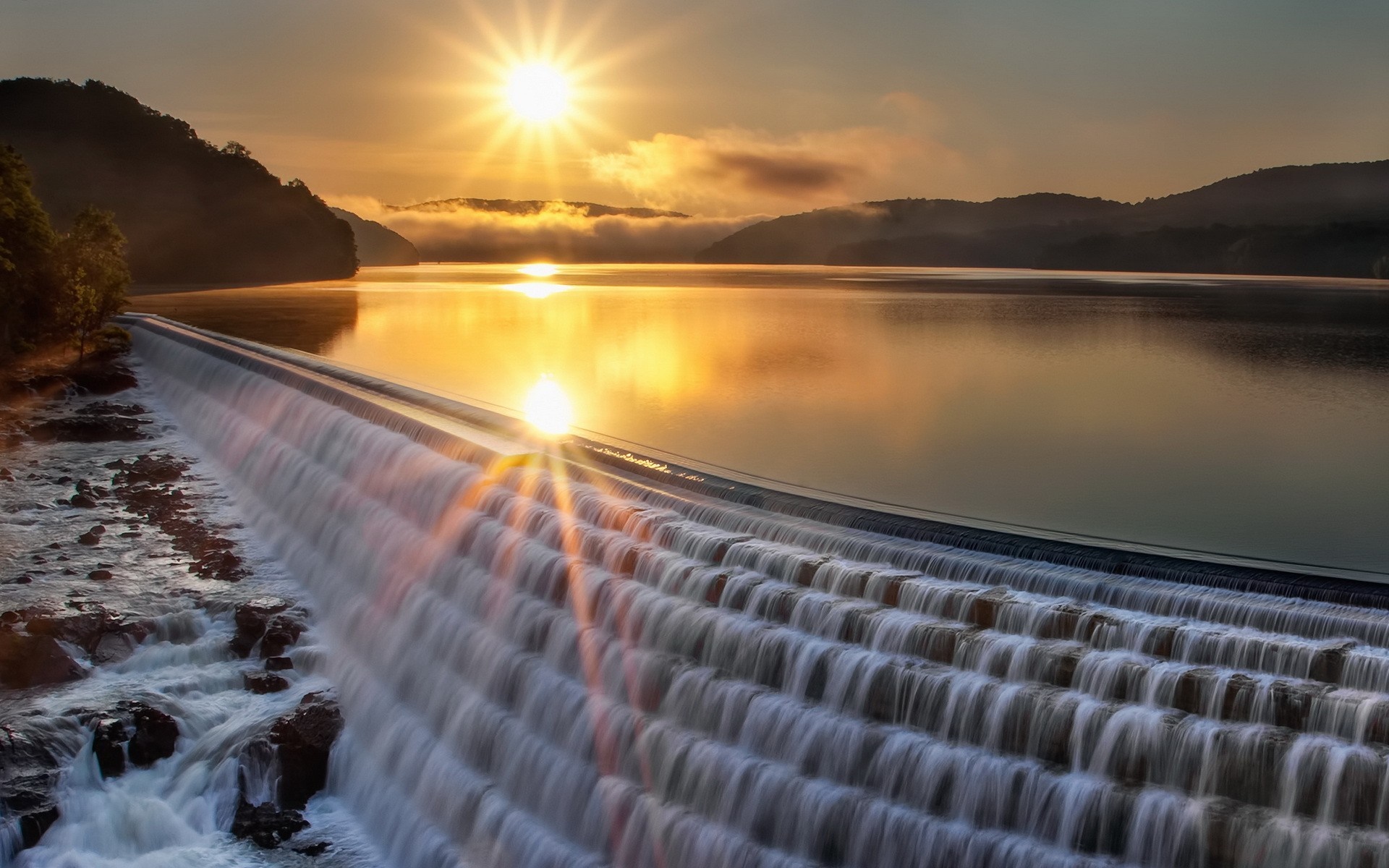Sunrise over a dam with water cascading down HD Wallpaper
