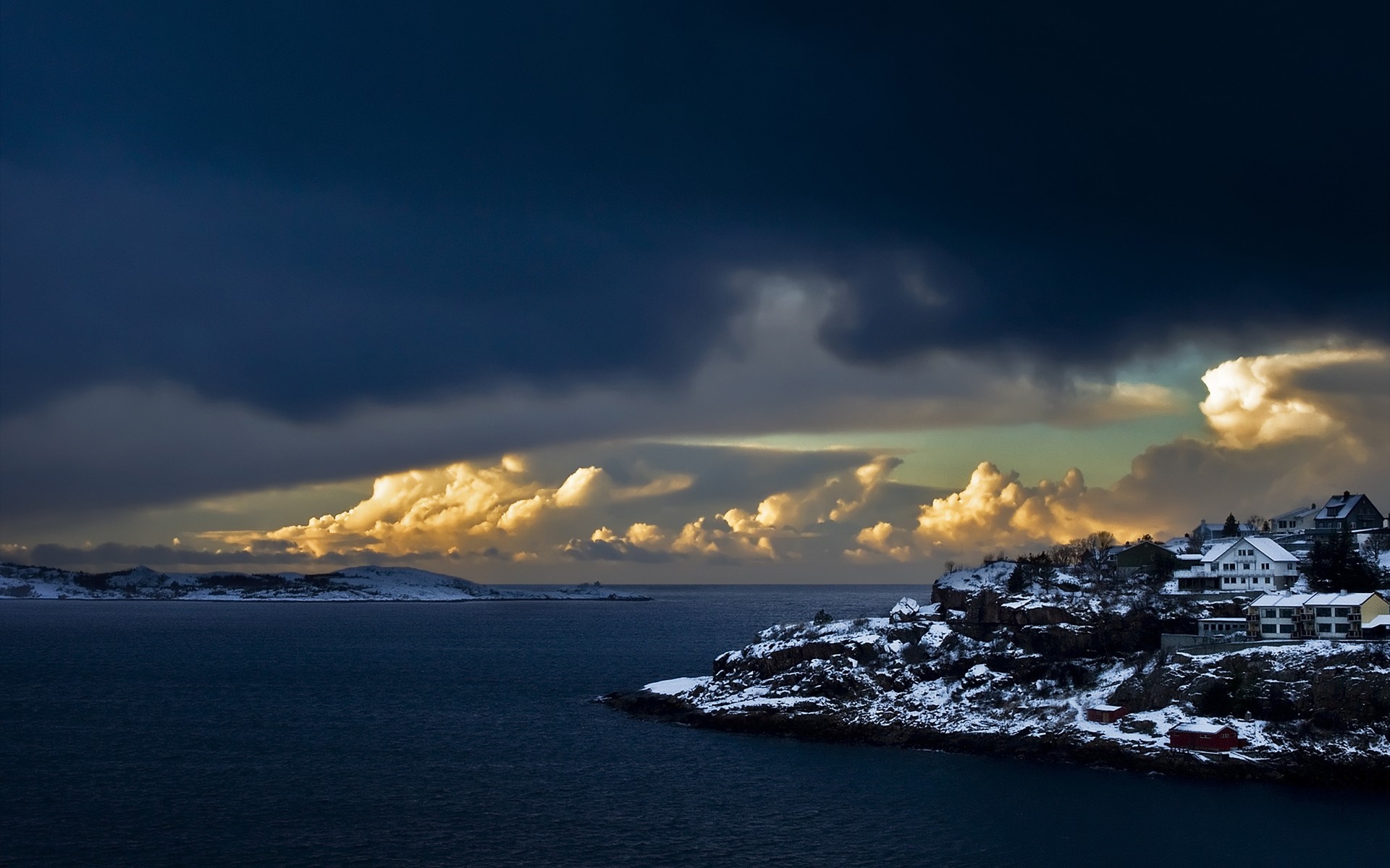 Snowy coastal village under dramatic clouds at sunset HD Wallpaper