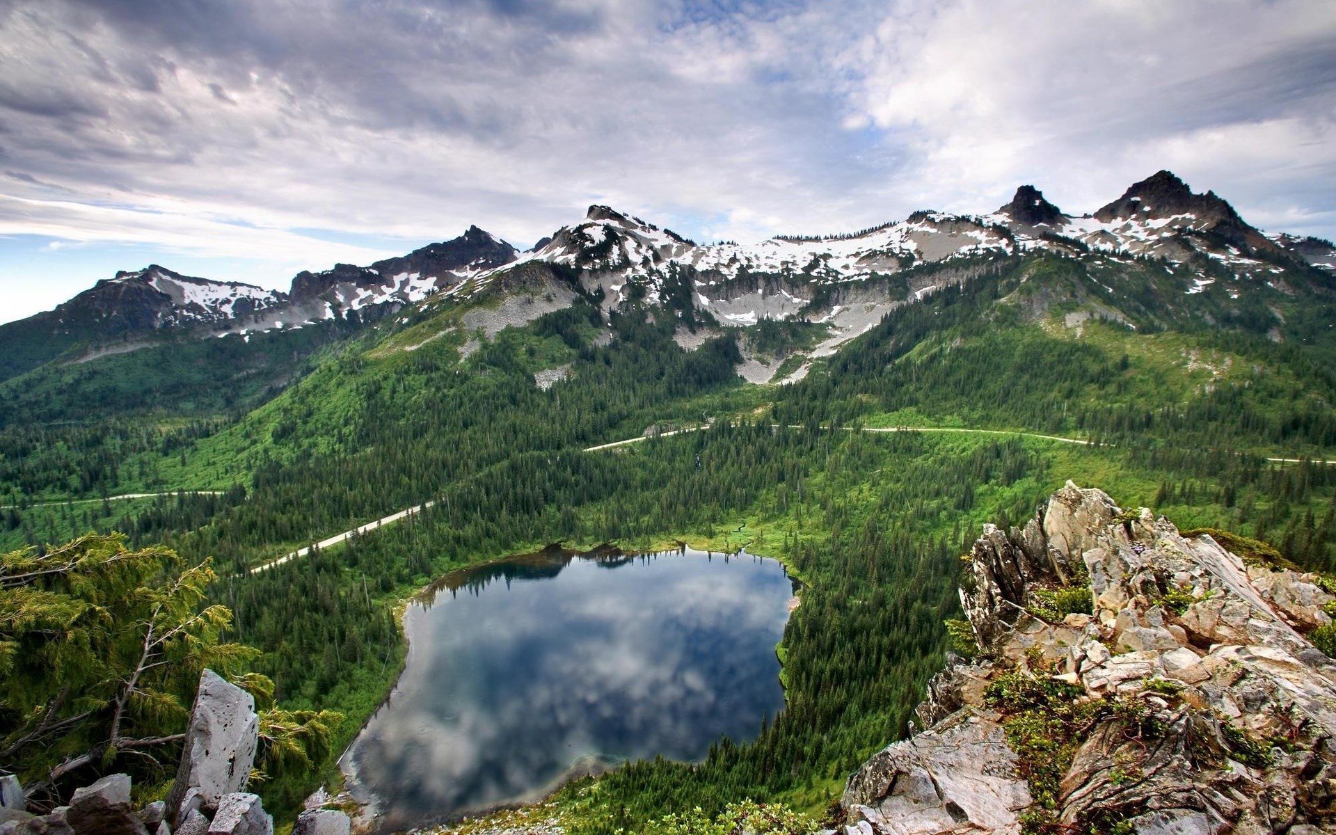 Mountain lake surrounded by evergreen forest and snow-capped peaks HD Wallpaper