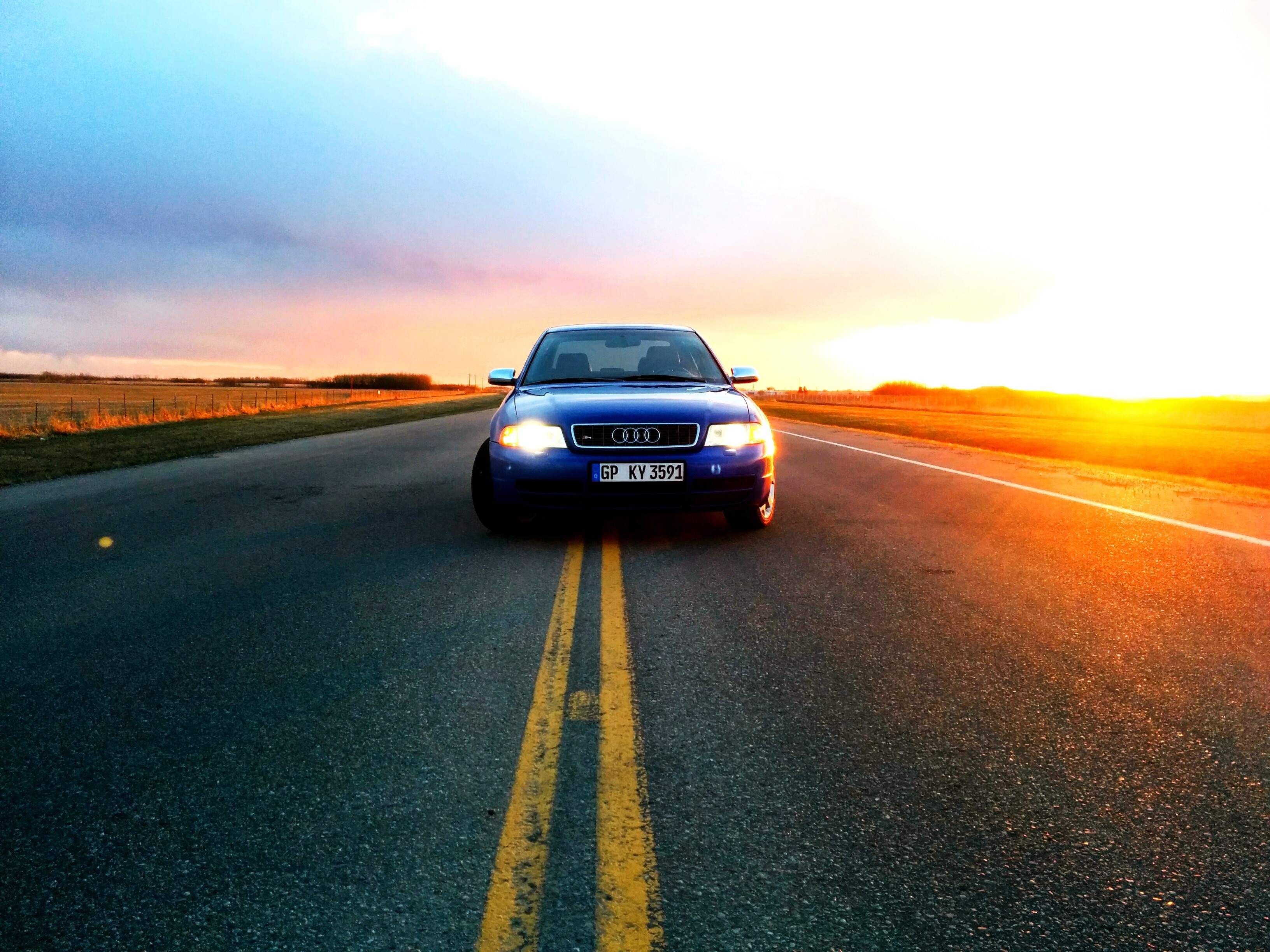 Blue Audi driving on a road at sunset HD Wallpaper