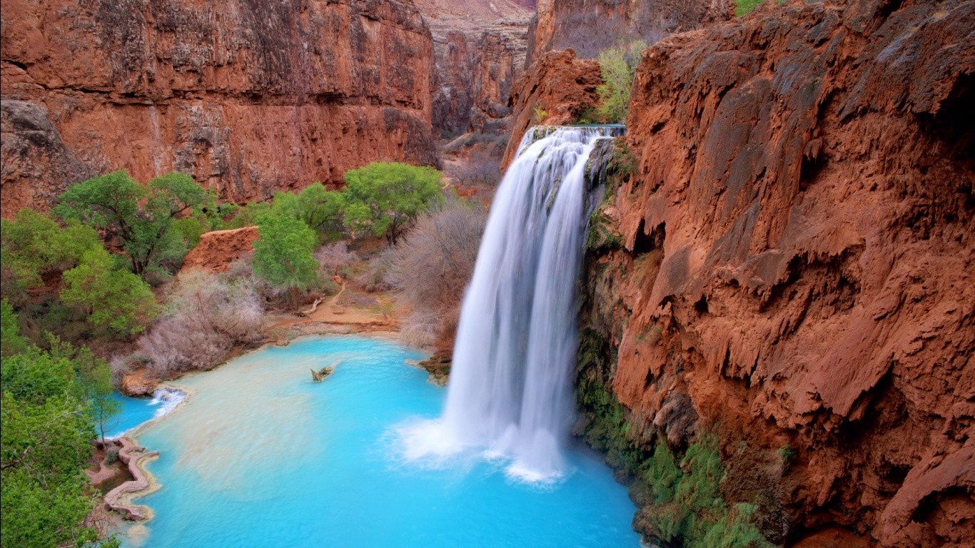 Waterfall cascading into a bright blue pool in a red rock canyon HD Wallpaper