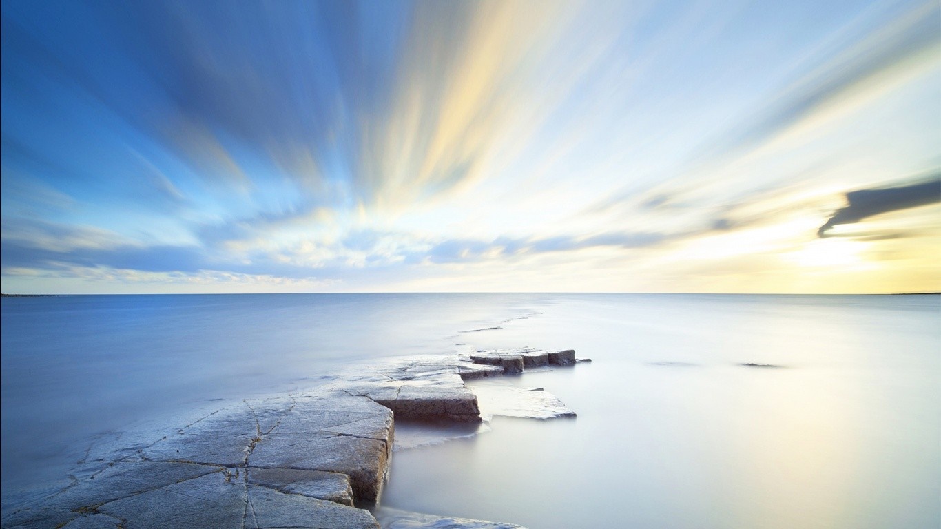 Long exposure of sea and sky with rocky shore HD Wallpaper