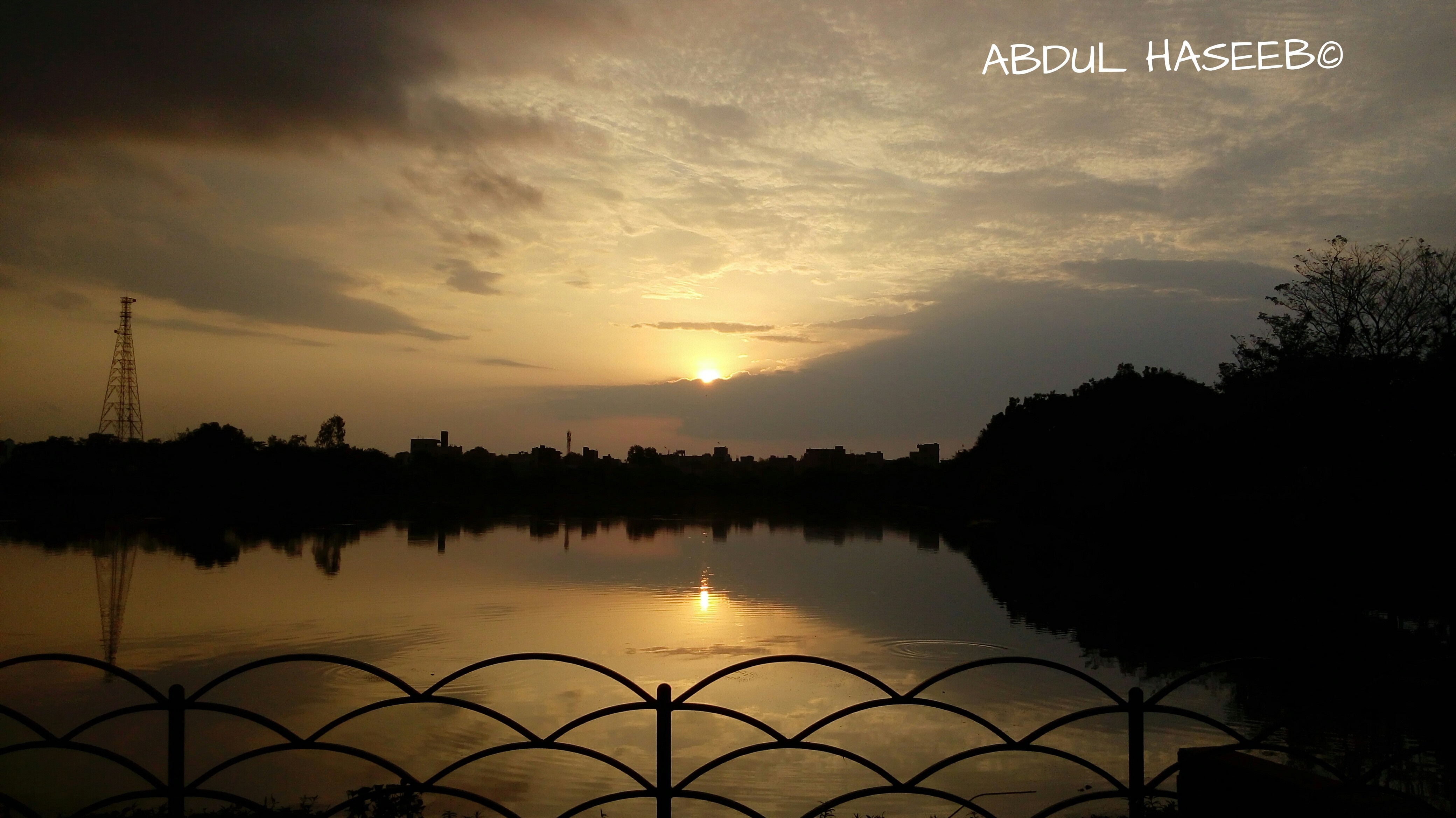 Sunset over a lake with a silhouette of a city and a tower HD Wallpaper