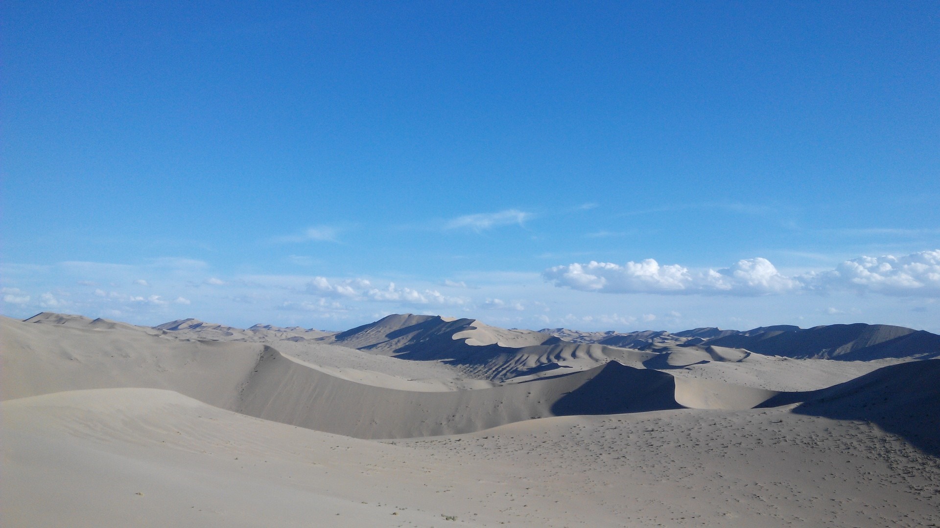 Vast desert landscape with rolling sand dunes under a blue sky HD Wallpaper