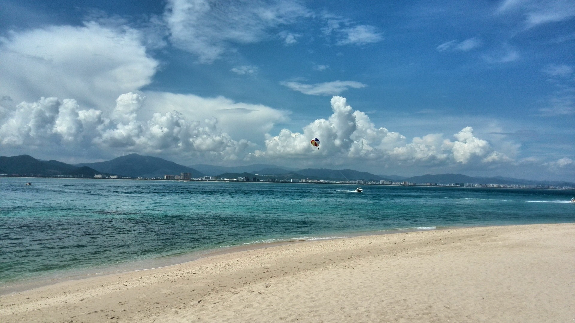 Beach with parasailer and distant city skyline HD Wallpaper