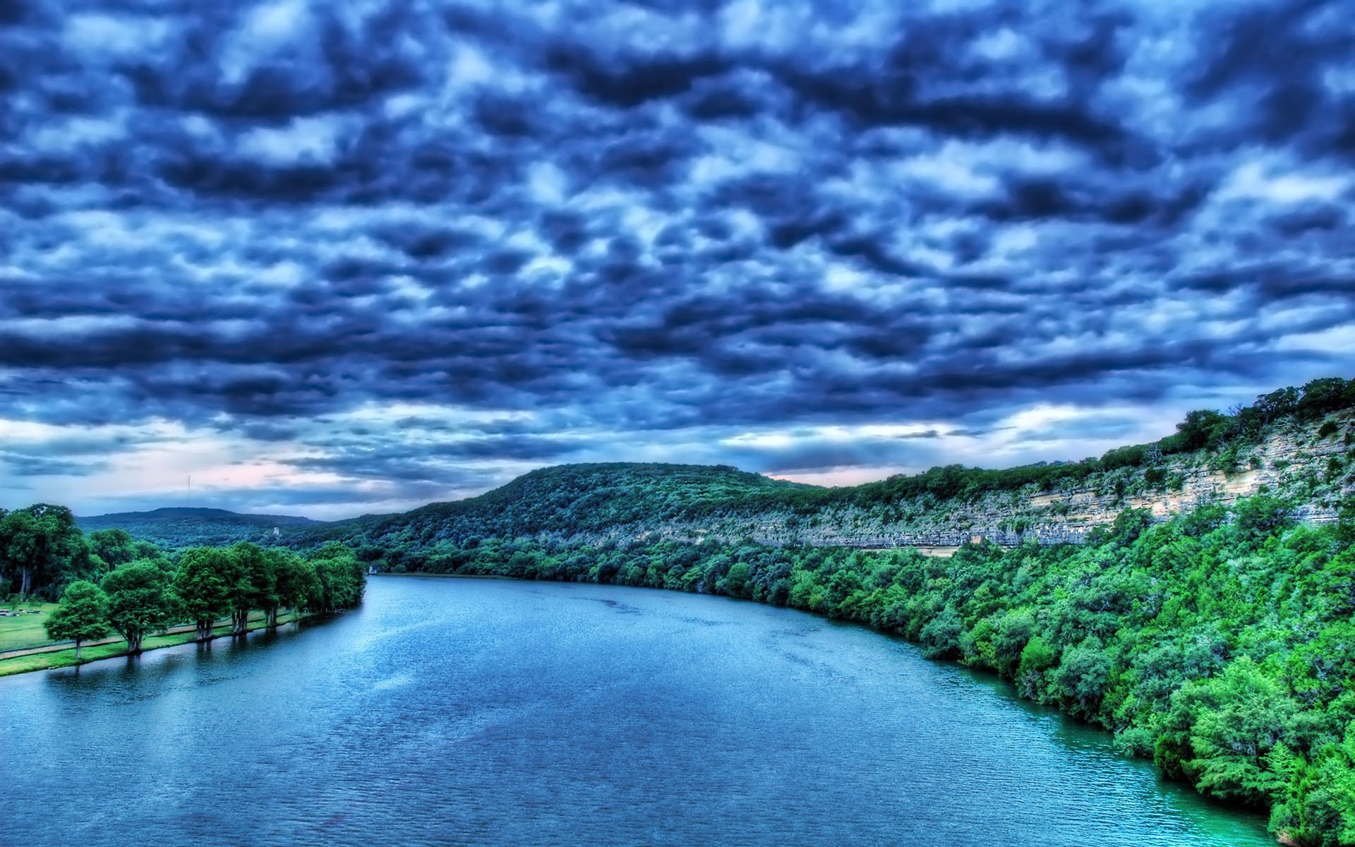 River flowing through a forested landscape under a cloudy sky HD Wallpaper
