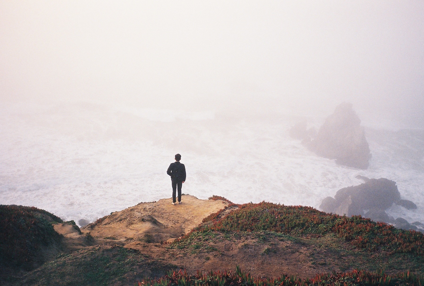 Person standing on a cliff overlooking a foggy sea HD Wallpaper