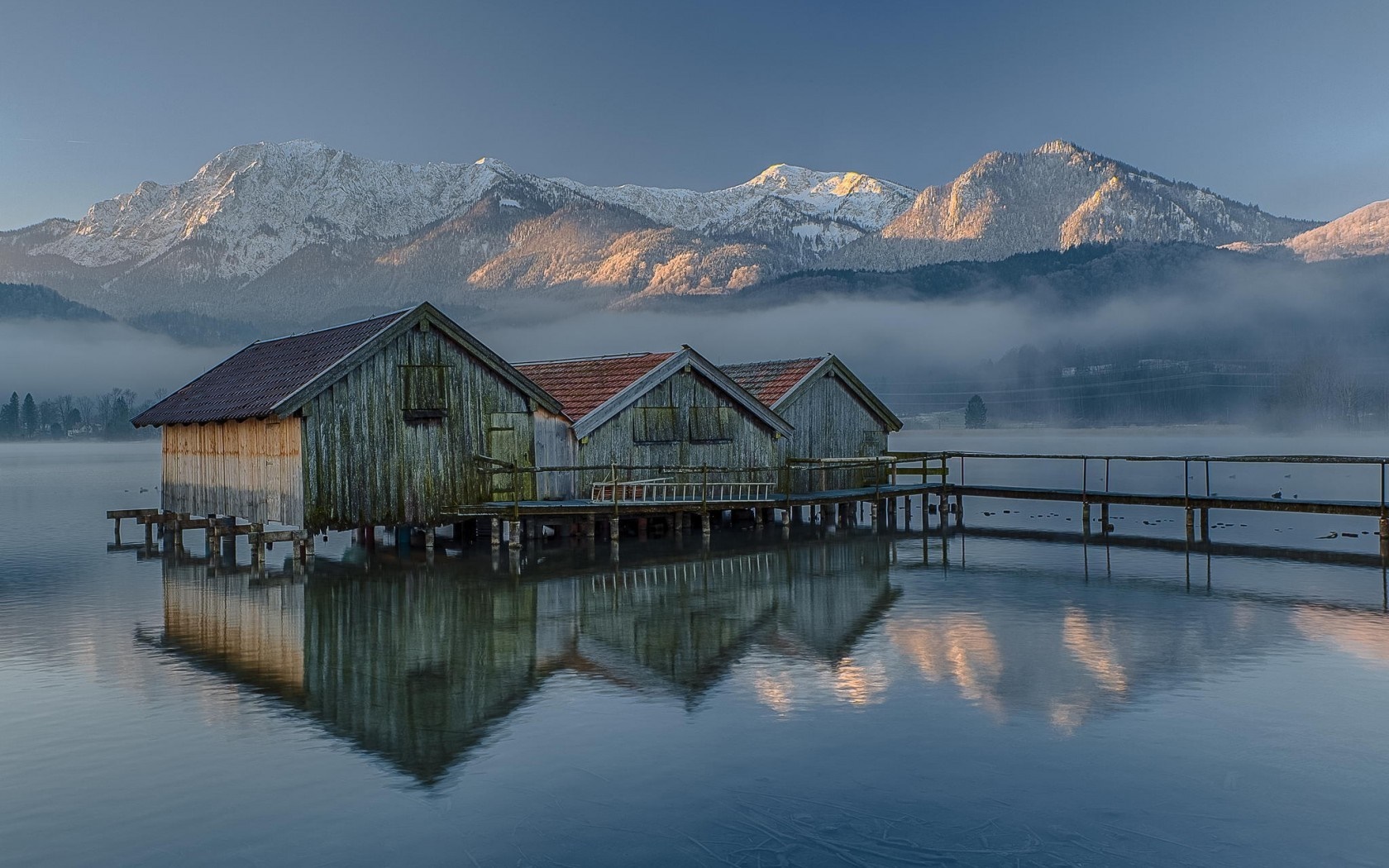 Wooden boathouses on a misty lake with snow-capped mountains HD Wallpaper