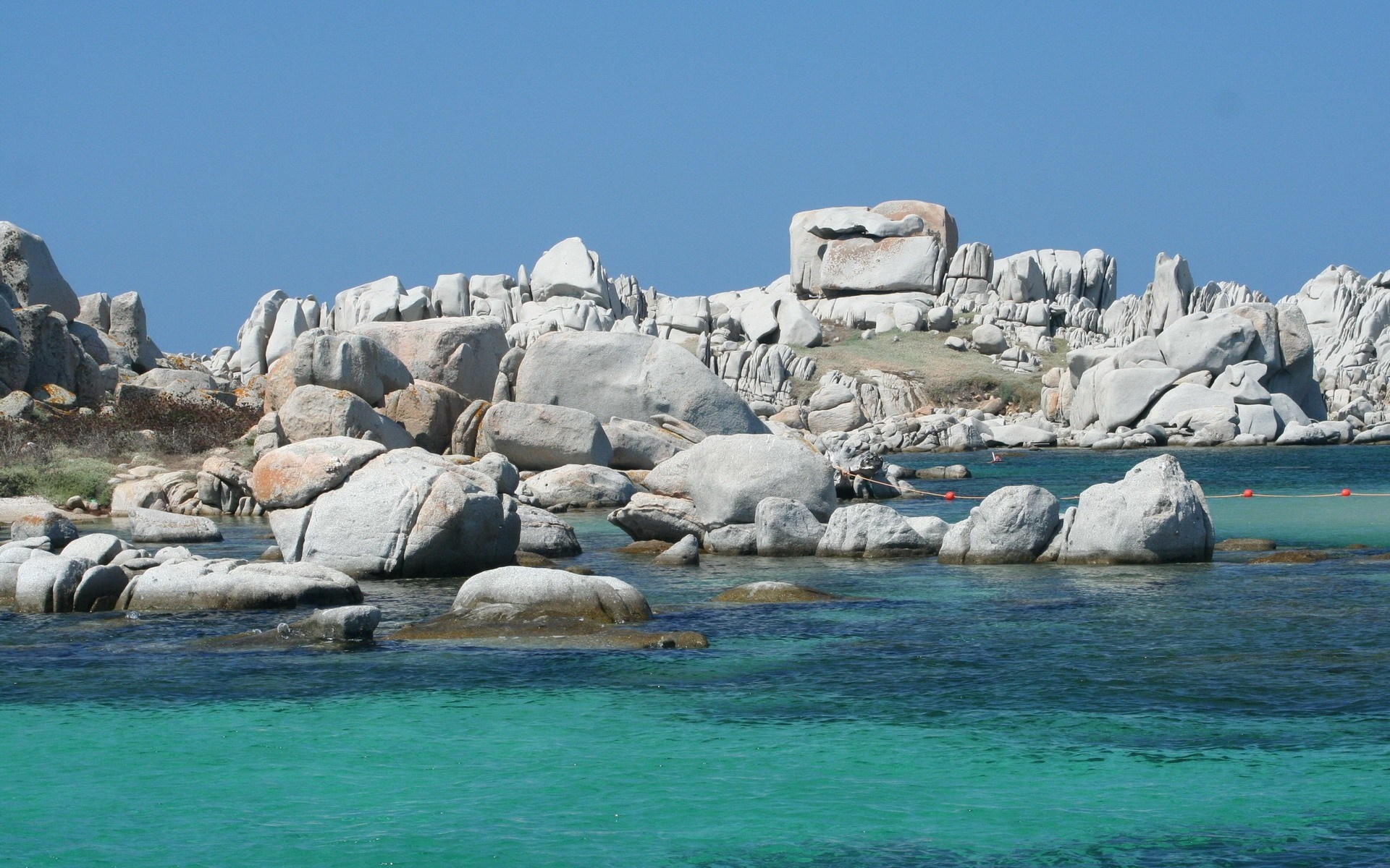 Rocky coast with turquoise water under a clear blue sky HD Wallpaper