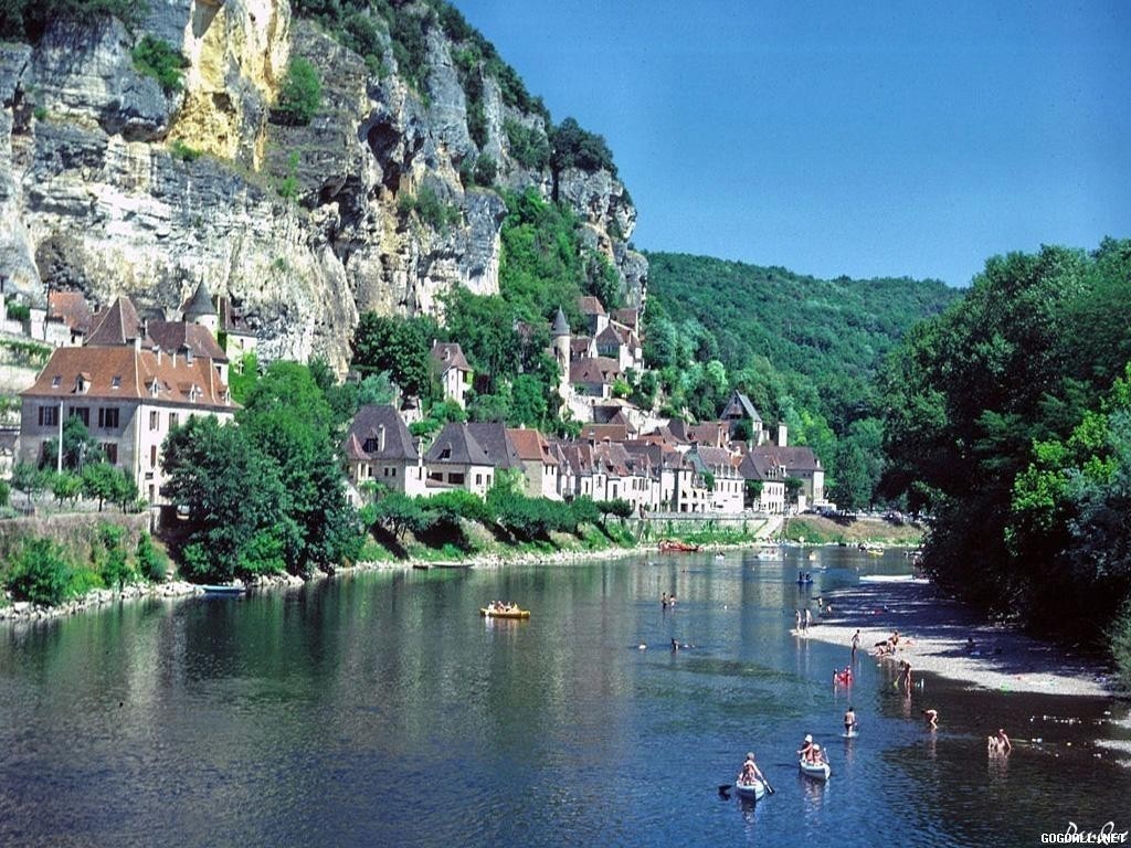 Village on a cliff overlooking a river with people swimming HD Wallpaper