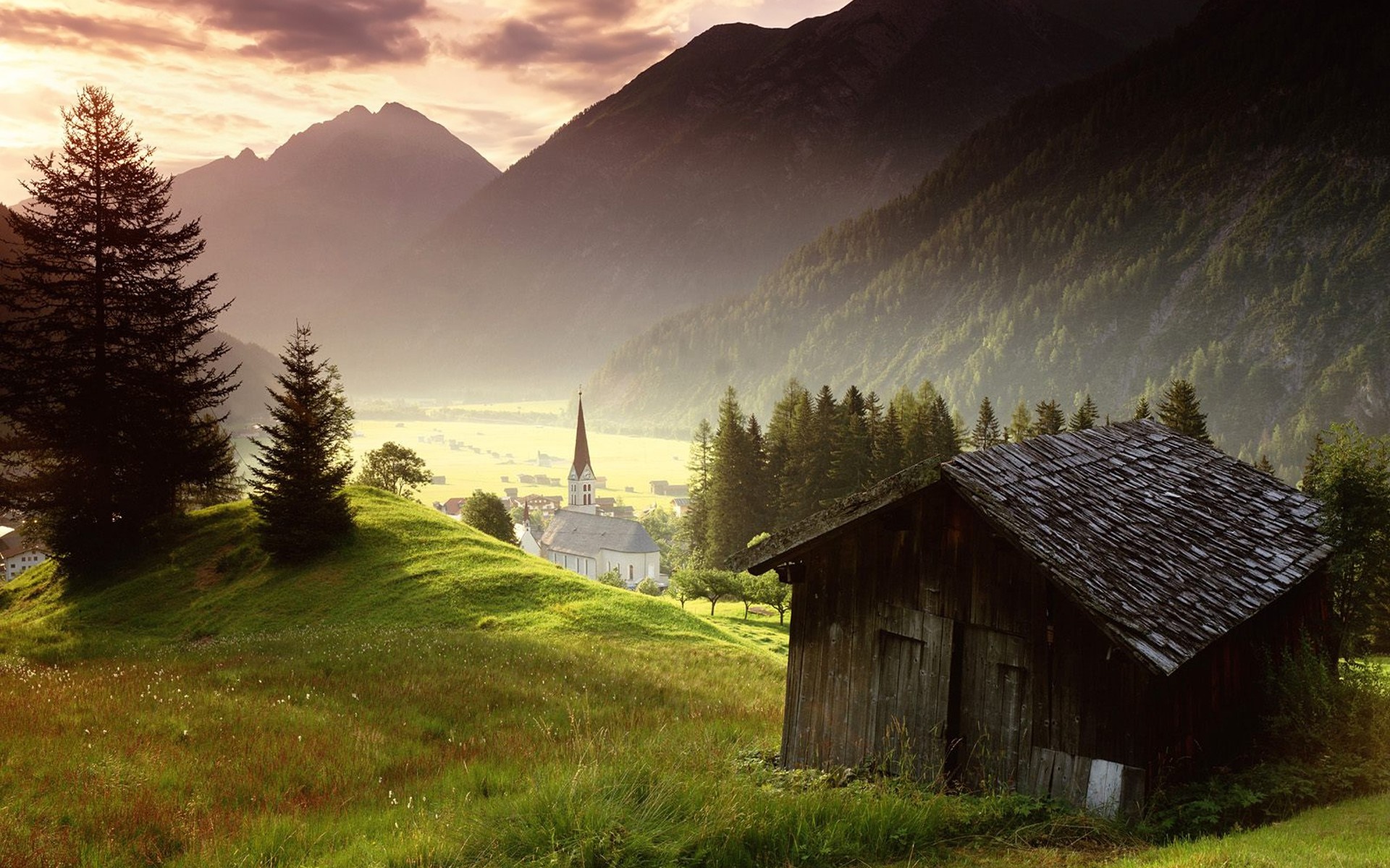 Mountain valley with church and wooden hut at sunrise HD Wallpaper