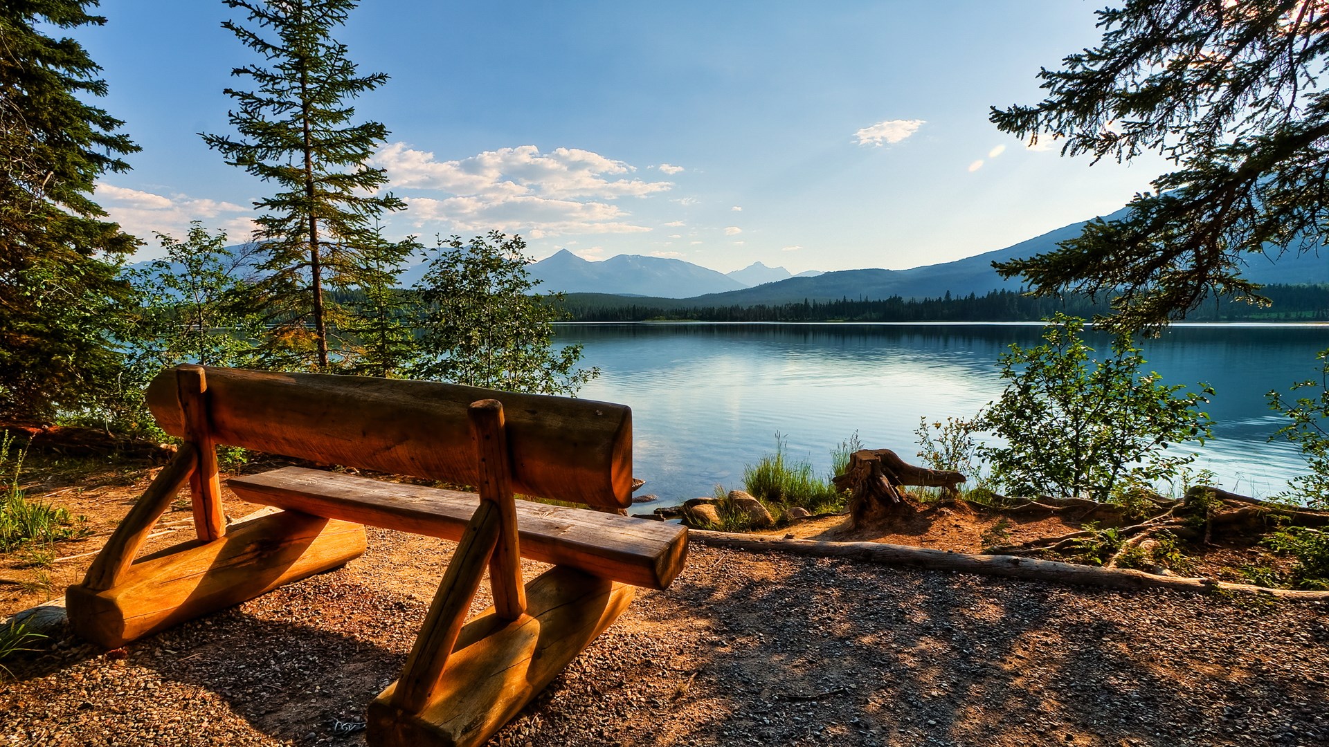 Wooden bench overlooking a calm lake and mountains HD Wallpaper