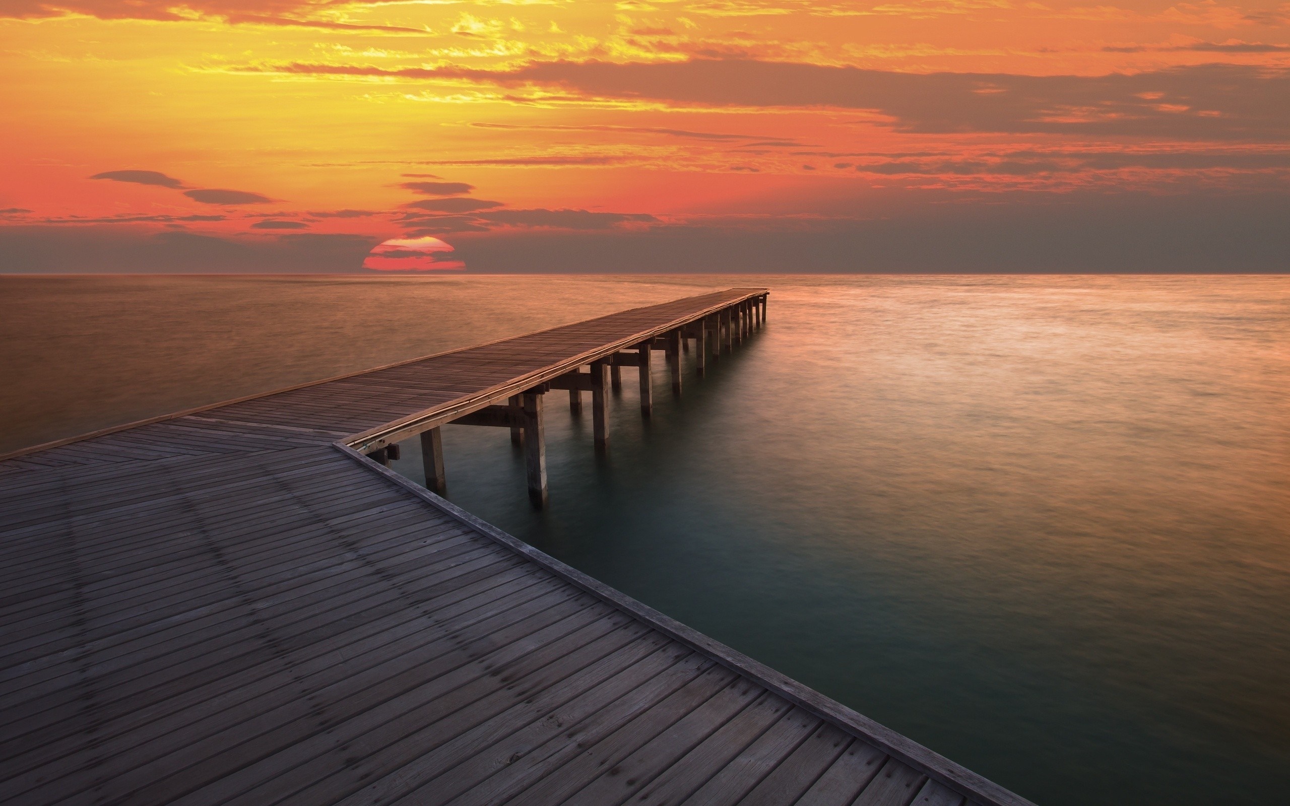 Wooden pier extending into the ocean at sunset HD Wallpaper