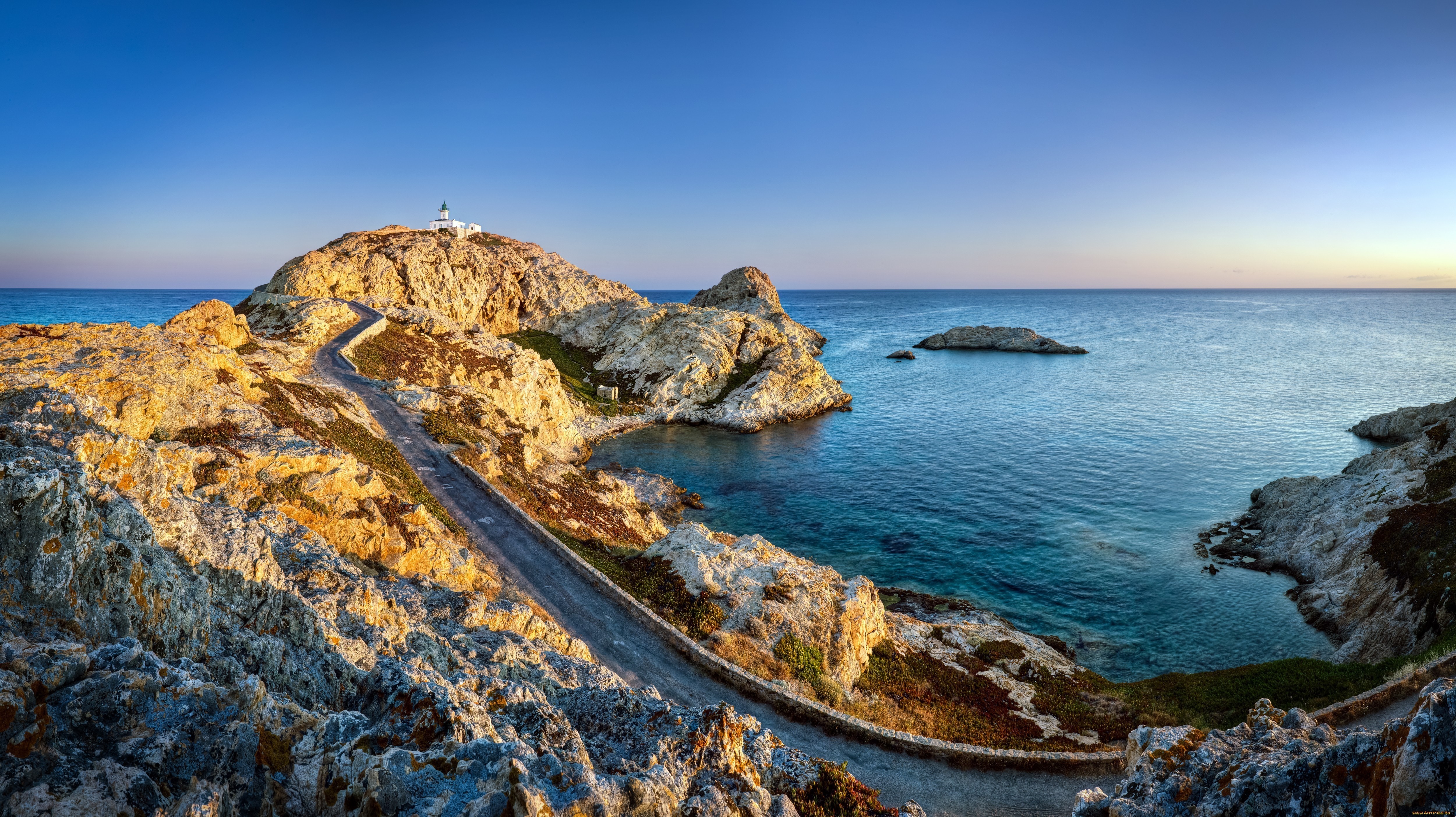 Coastal road leading to a lighthouse on a rocky island HD Wallpaper