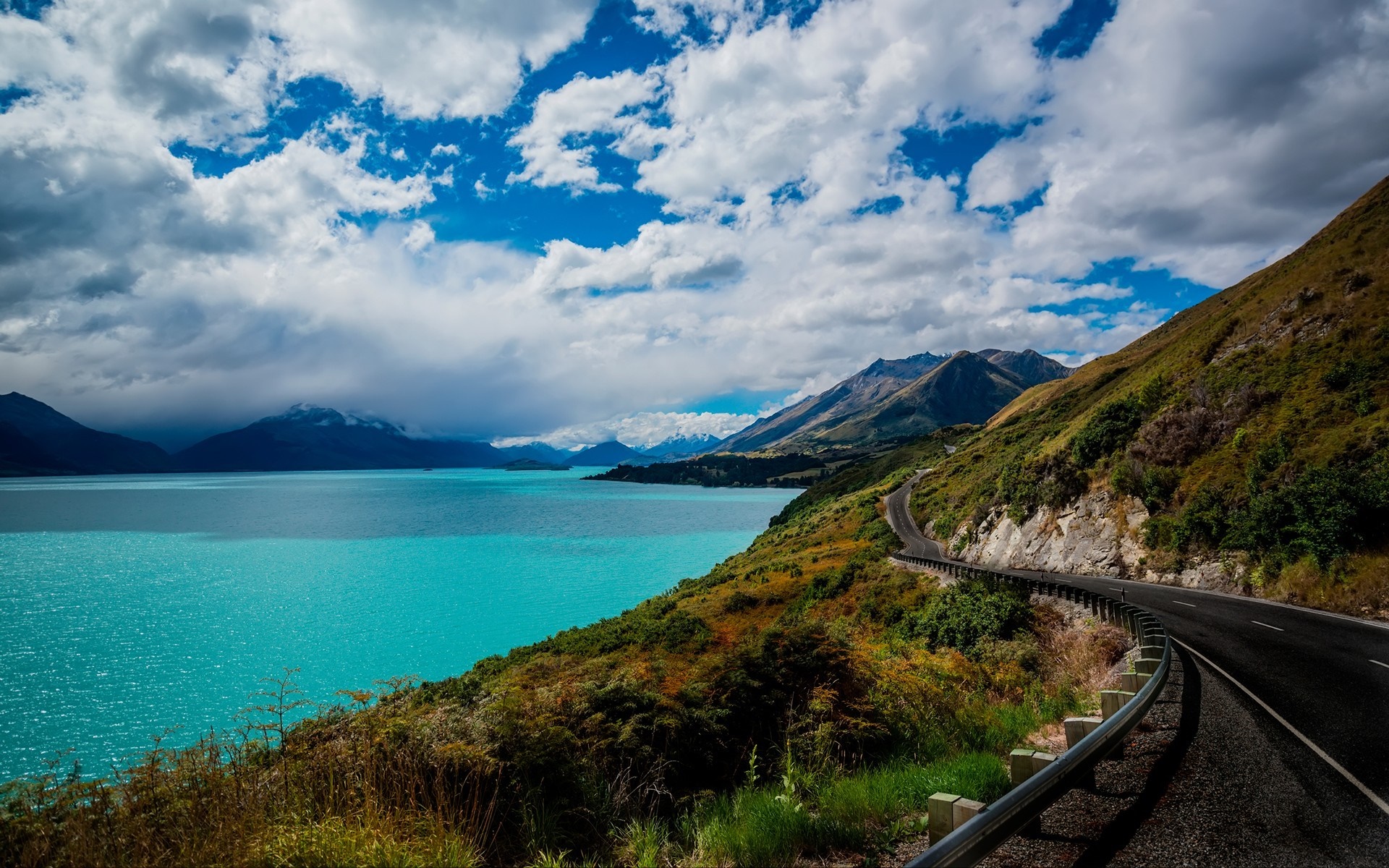 Winding road along a turquoise lake and mountains HD Wallpaper