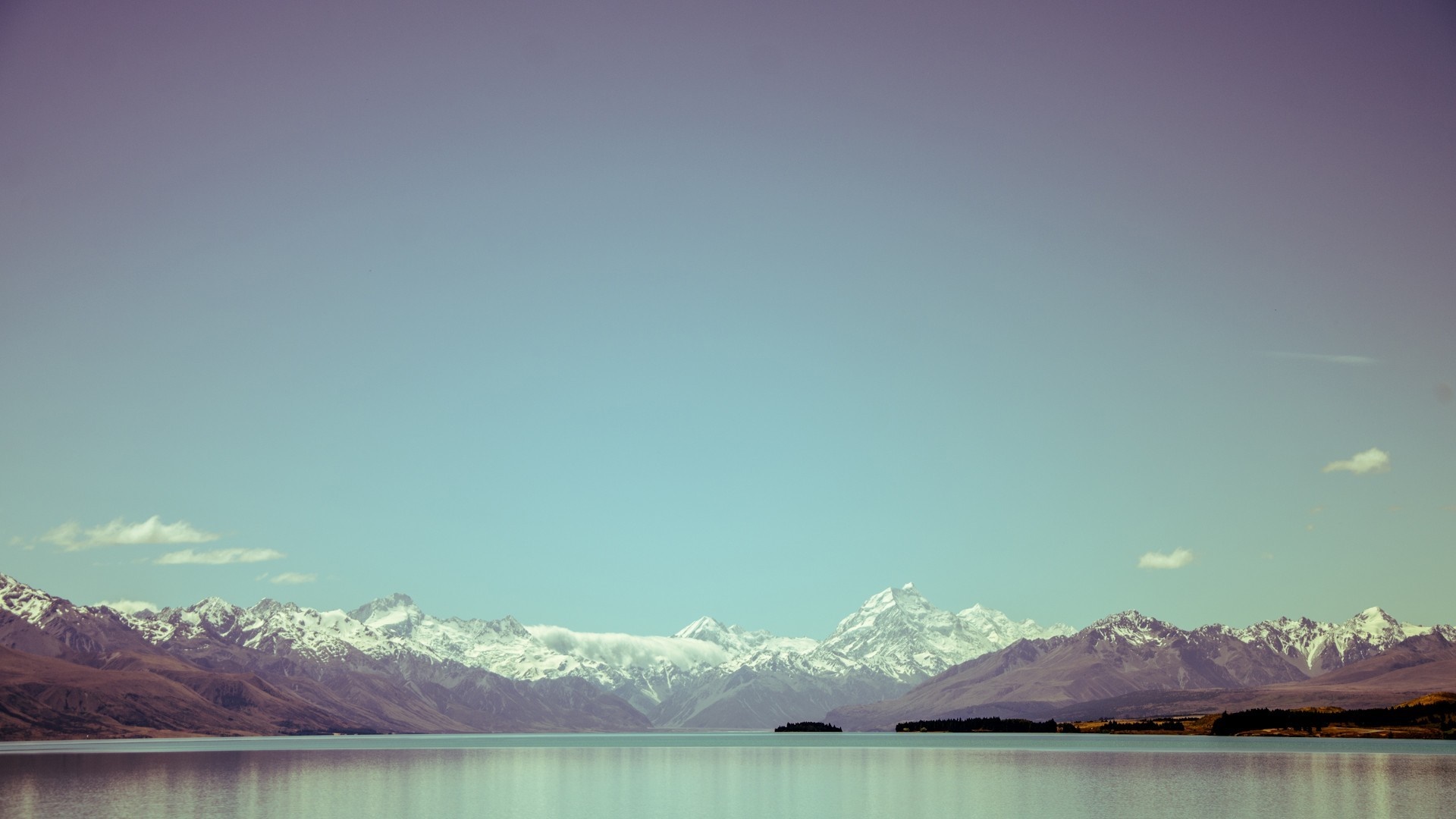 Snow-capped mountains reflected in a calm lake under a gradient sky HD Wallpaper