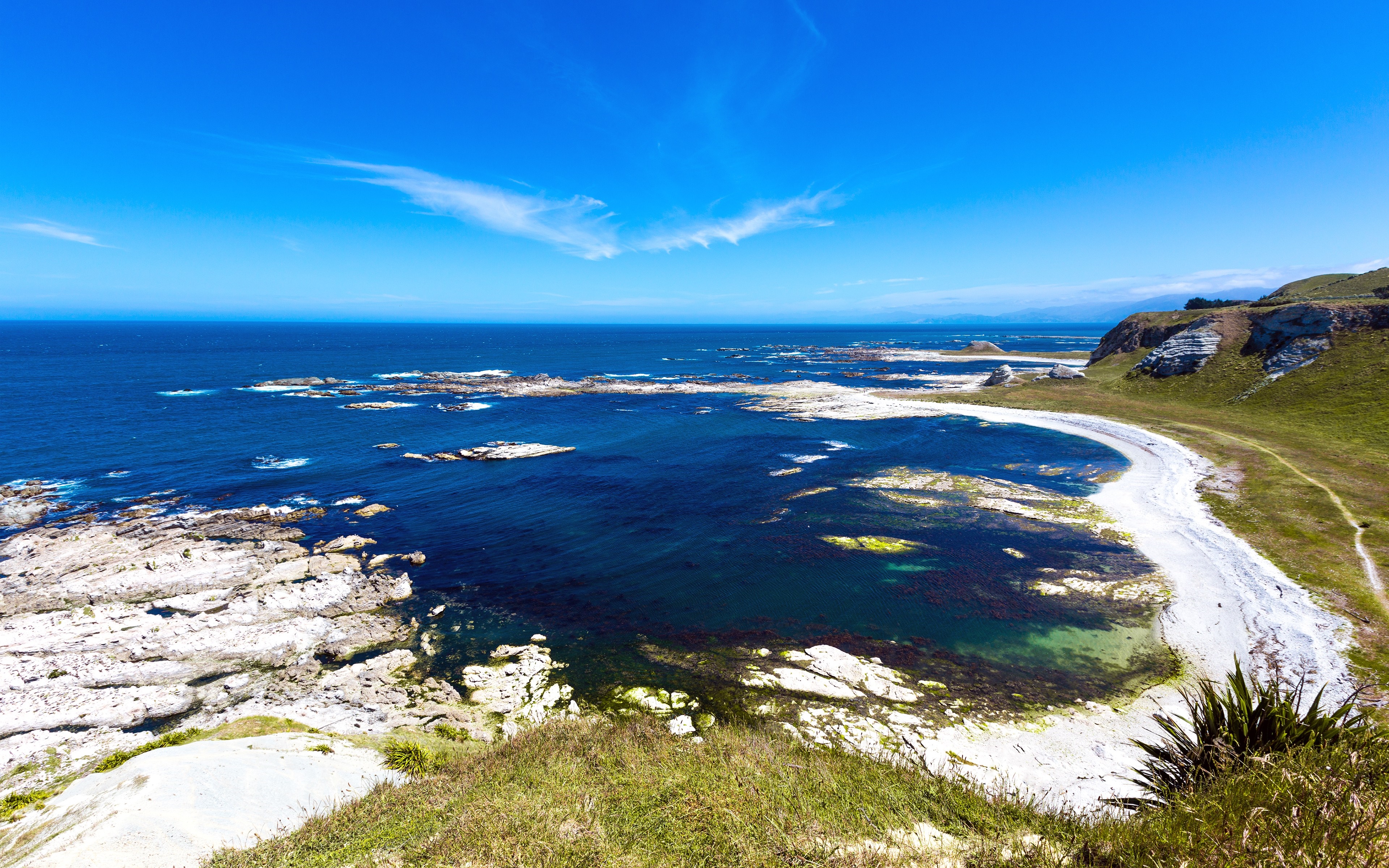 Coastal landscape with rocky shore and blue ocean under a clear sky HD Wallpaper
