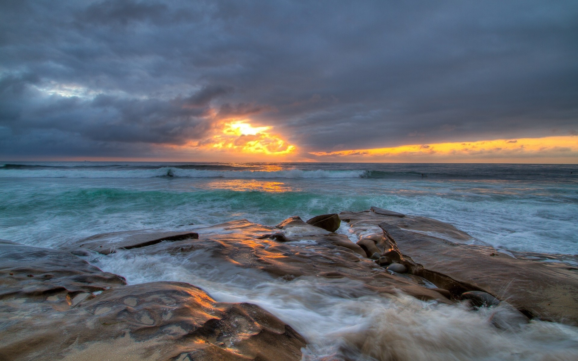 Sunset over the ocean with waves crashing on rocks HD Wallpaper