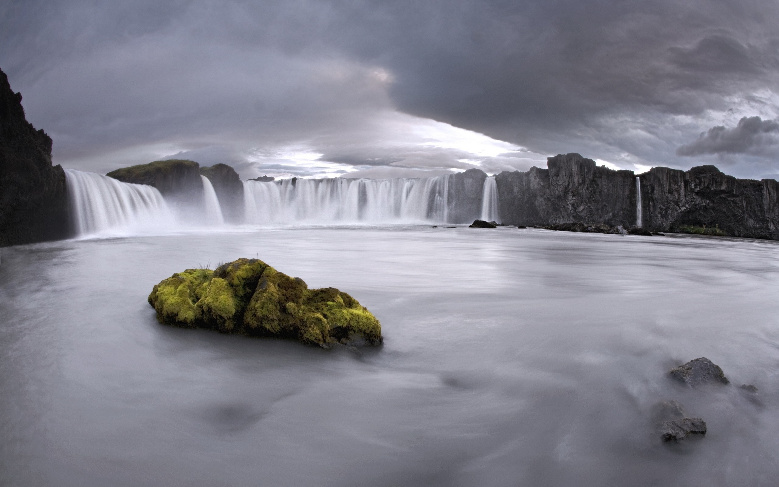 Wide waterfall with mossy rock in foreground under cloudy sky HD Wallpaper