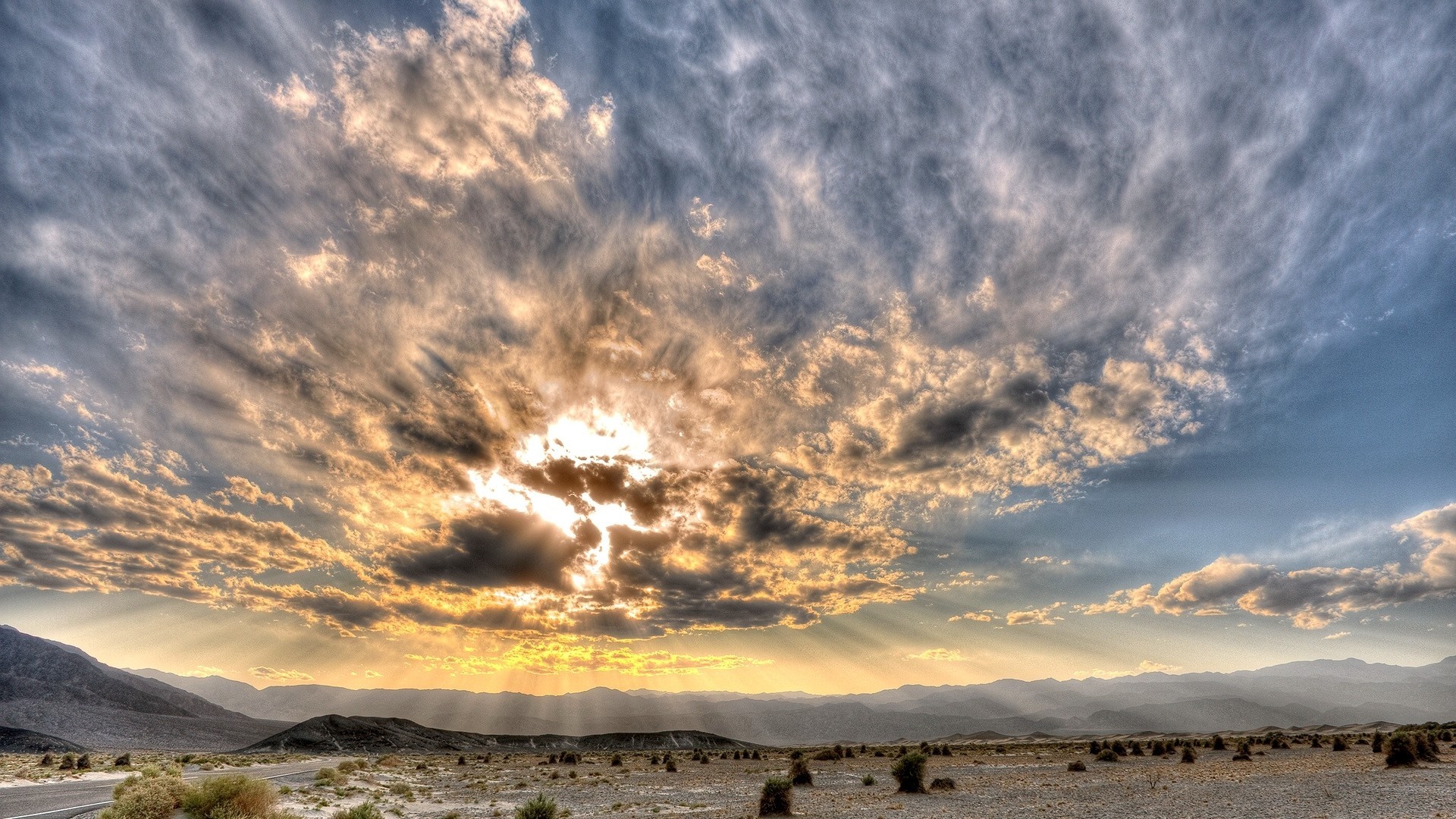 Sunlight breaking through clouds over a desert landscape HD Wallpaper