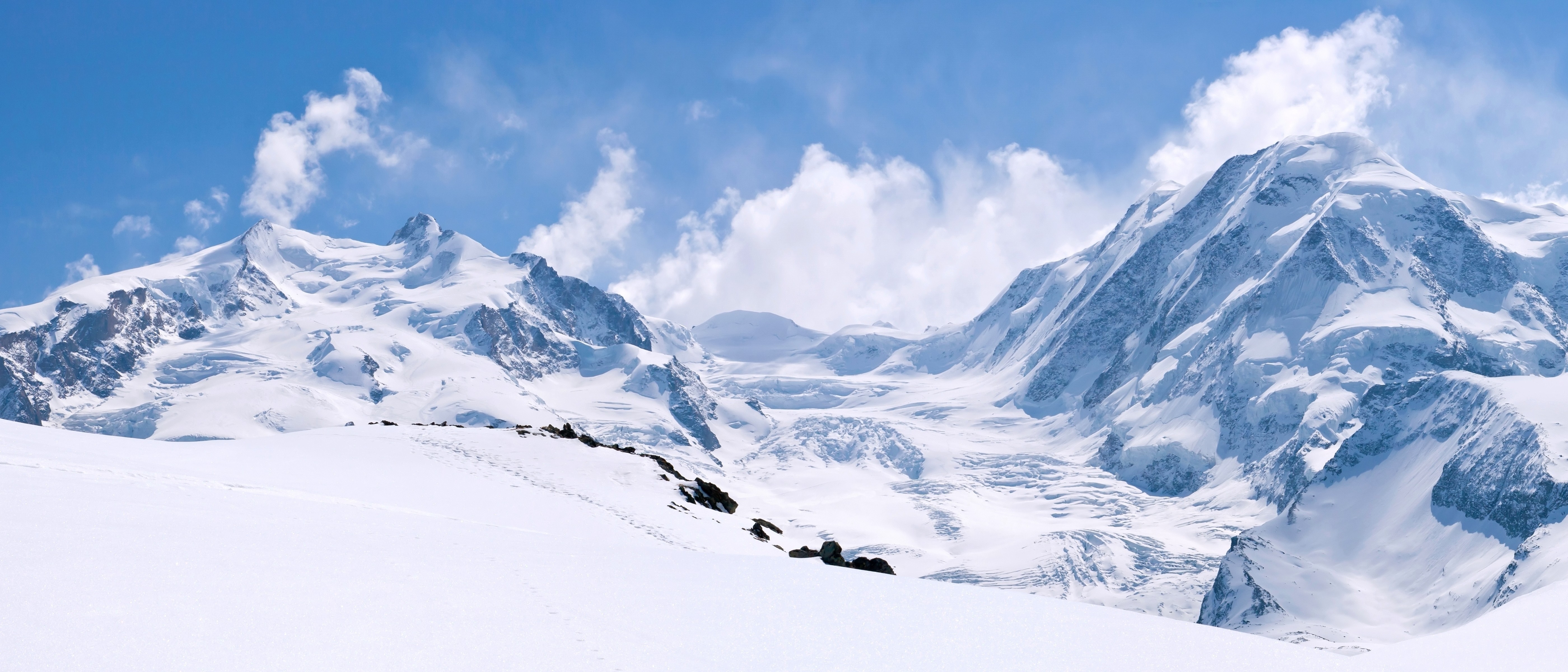 Snow-covered mountains under a blue sky with clouds HD Wallpaper