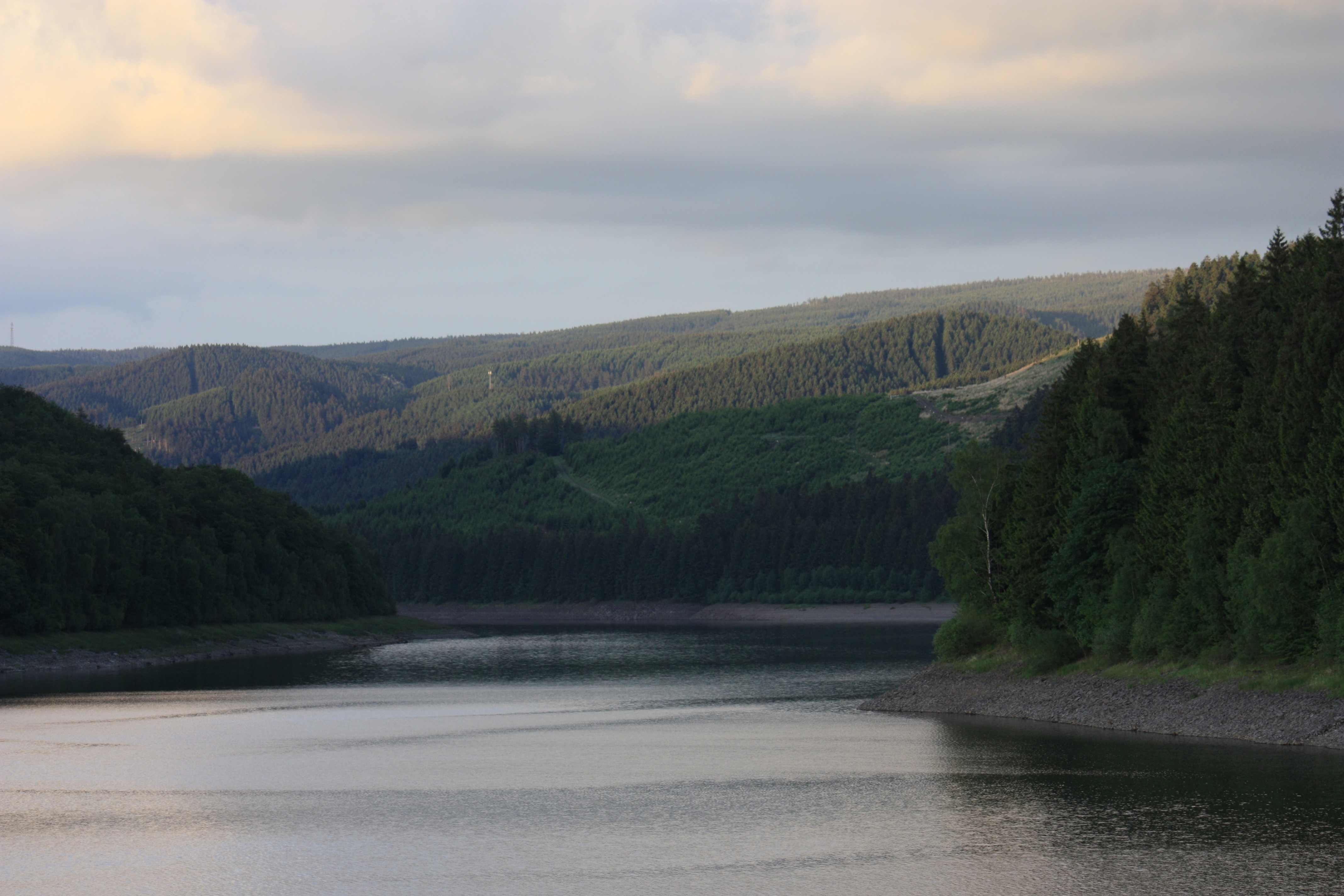 Reservoir surrounded by forested hills under a cloudy sky HD Wallpaper