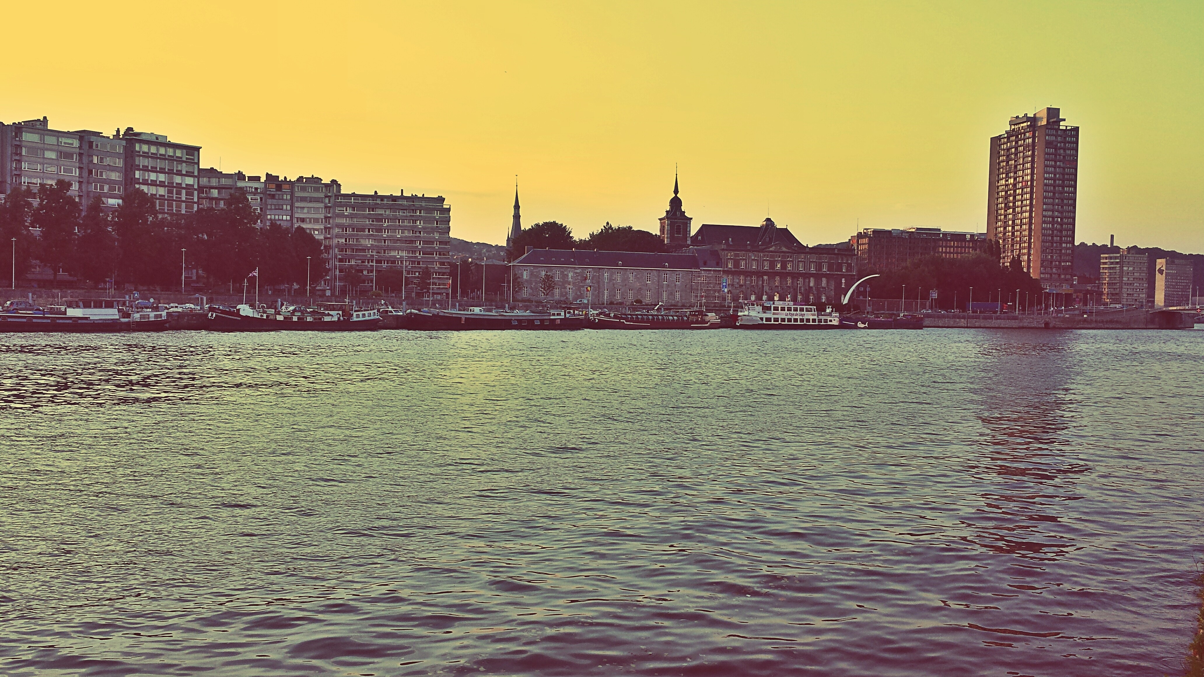 Cityscape with buildings and boats on a river at sunset HD Wallpaper