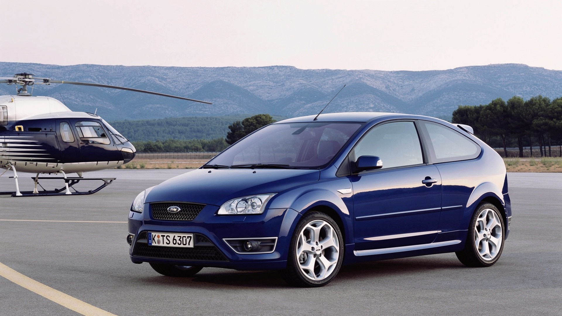 Blue Ford Focus ST parked next to a helicopter HD Wallpaper