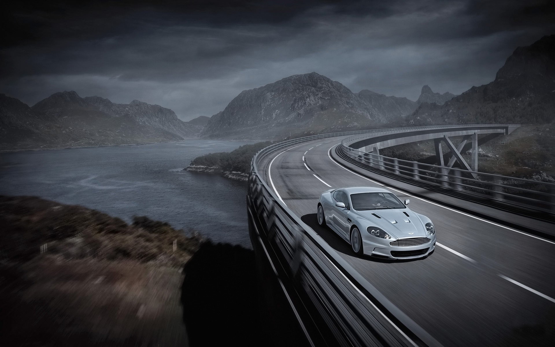 Silver Aston Martin DBS driving on a scenic highway HD Wallpaper