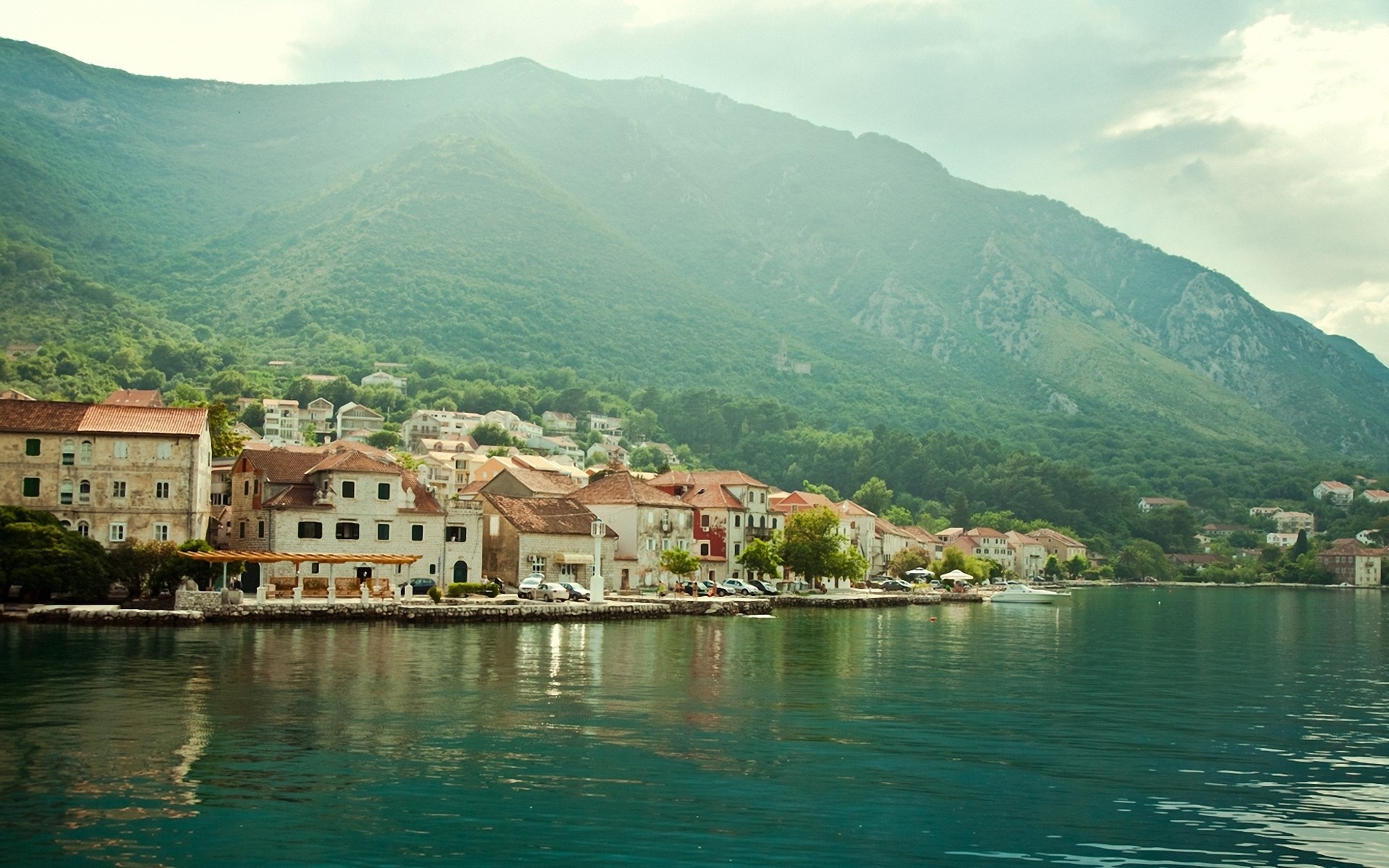 Coastal town nestled at the base of a lush mountain range HD Wallpaper