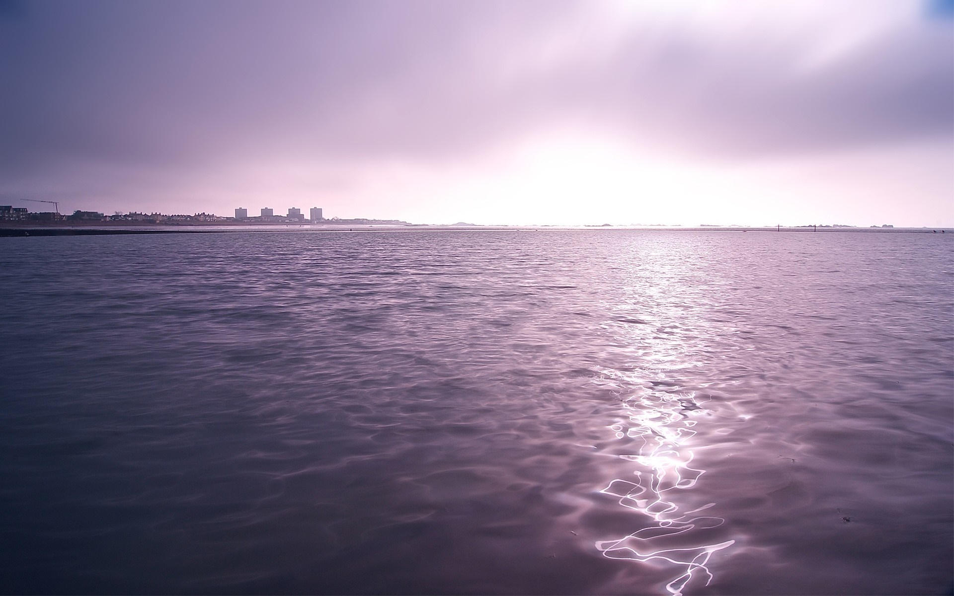 Water reflecting sunlight on the horizon with a city skyline HD Wallpaper