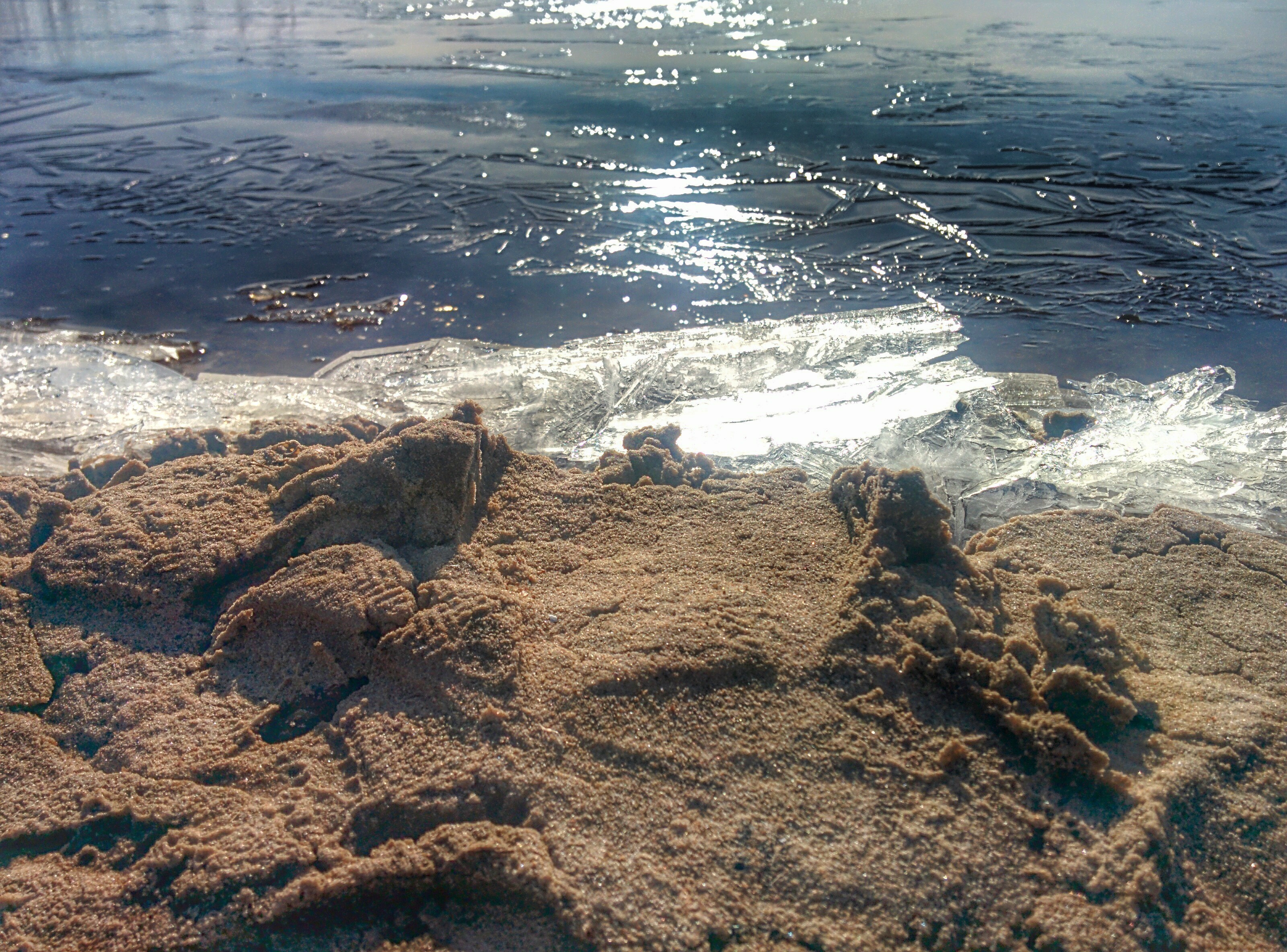 Sandy shore with ice and water reflecting sunlight HD Wallpaper