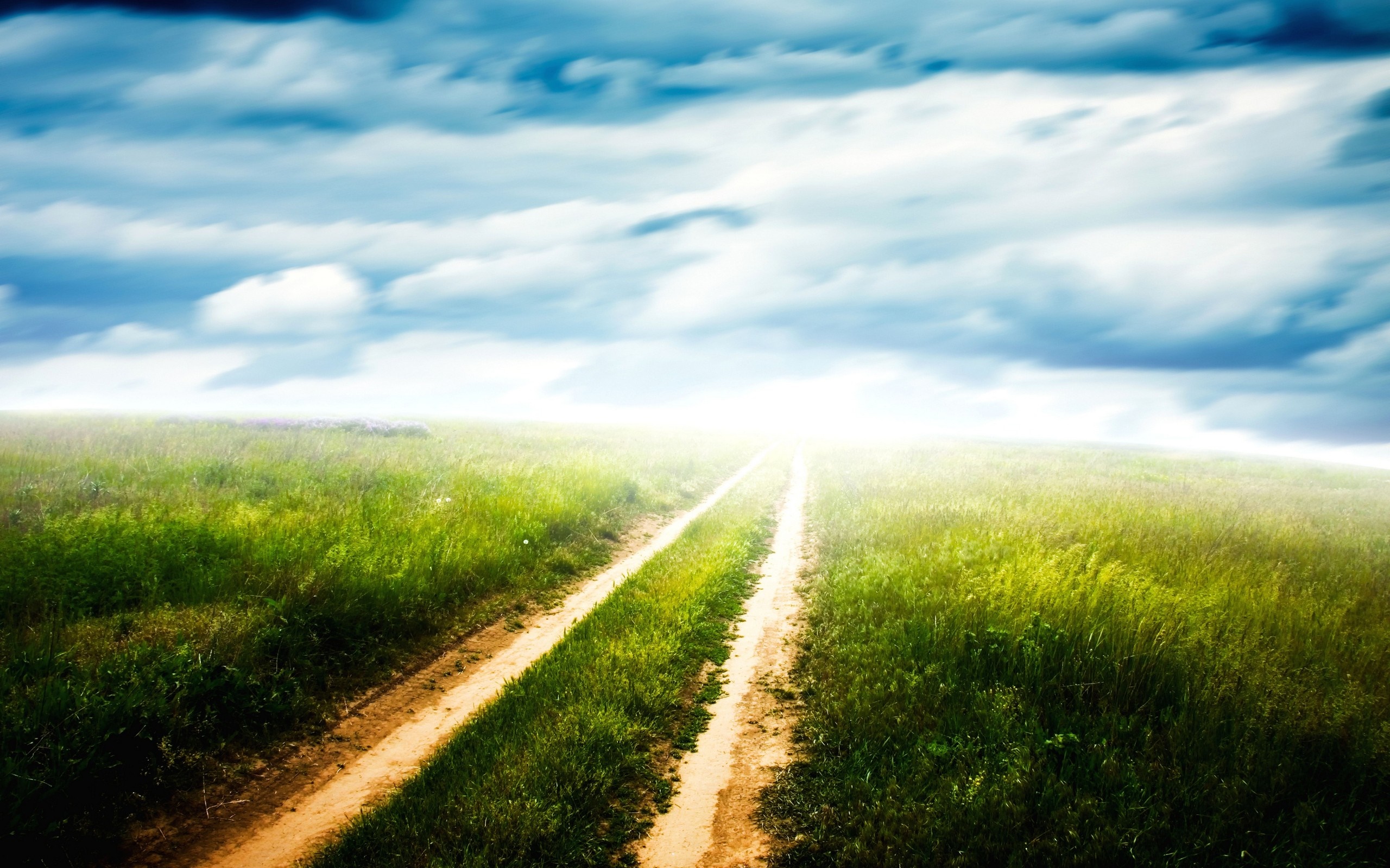 Dirt road through a green field under a cloudy sky HD Wallpaper