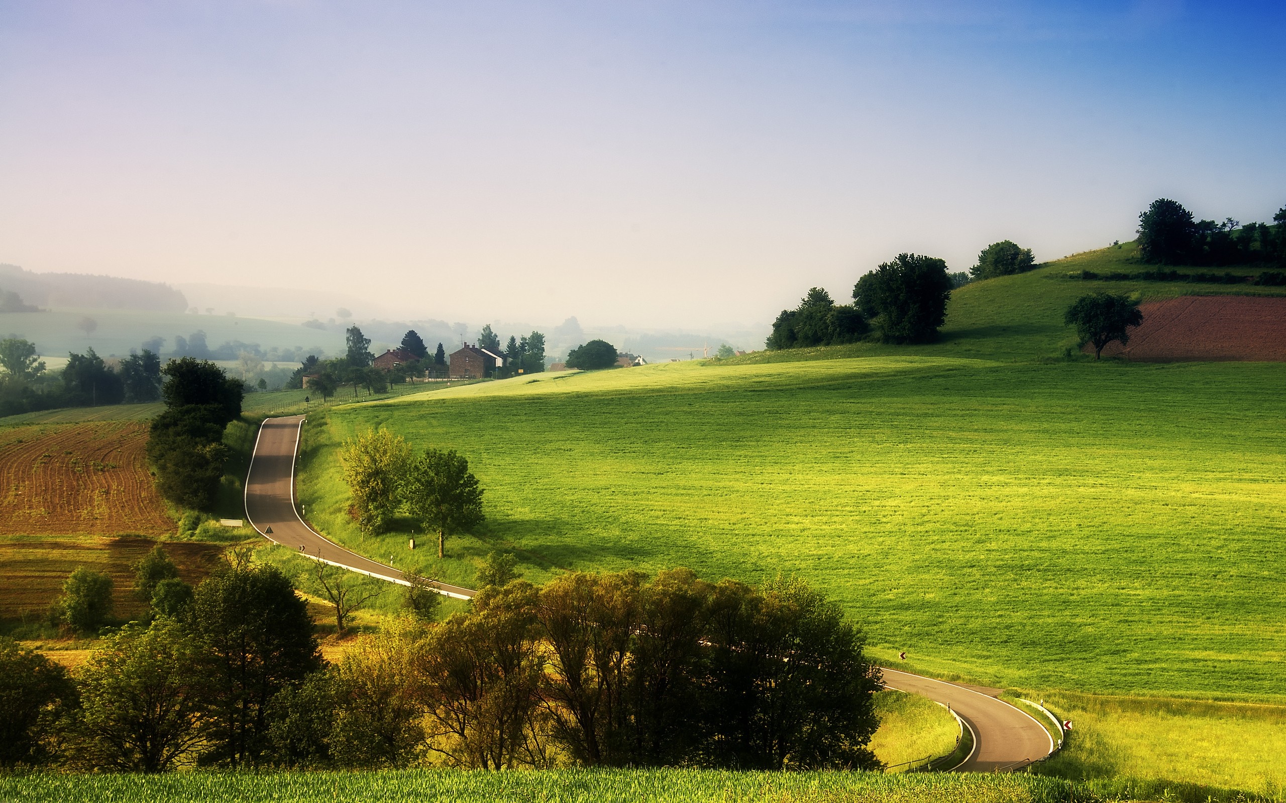 Rolling green hills with a winding road and farmhouses HD Wallpaper
