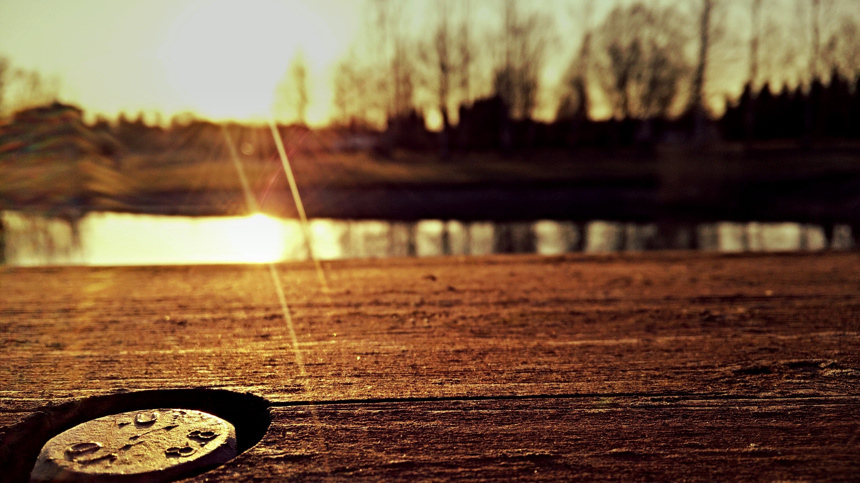 Close-up of a bolt on a wooden surface with sunset reflection on water HD Wallpaper