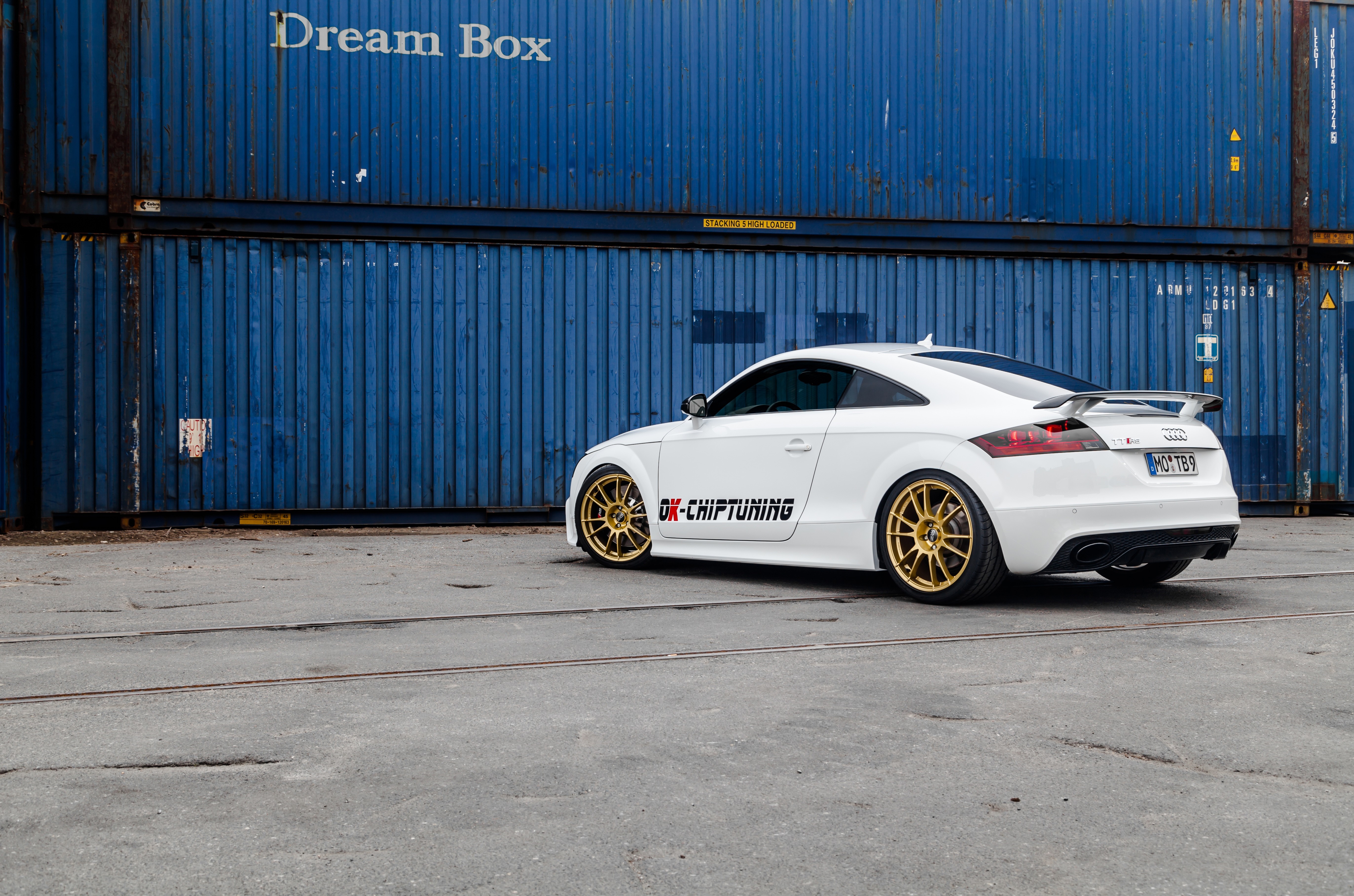 White Audi TT RS with gold wheels parked by blue shipping containers HD Wallpaper