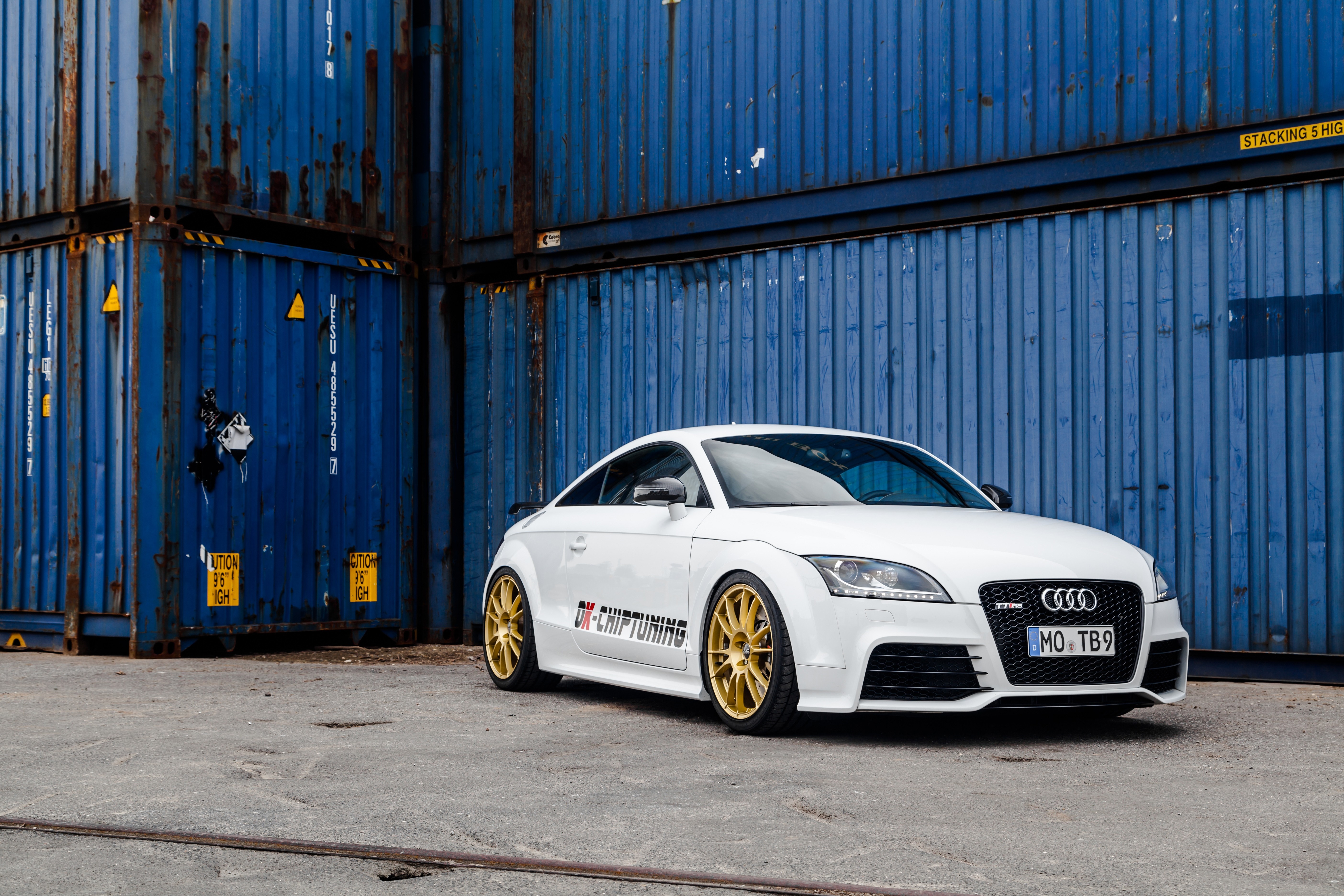White Audi TT RS with gold wheels parked by blue shipping containers HD Wallpaper