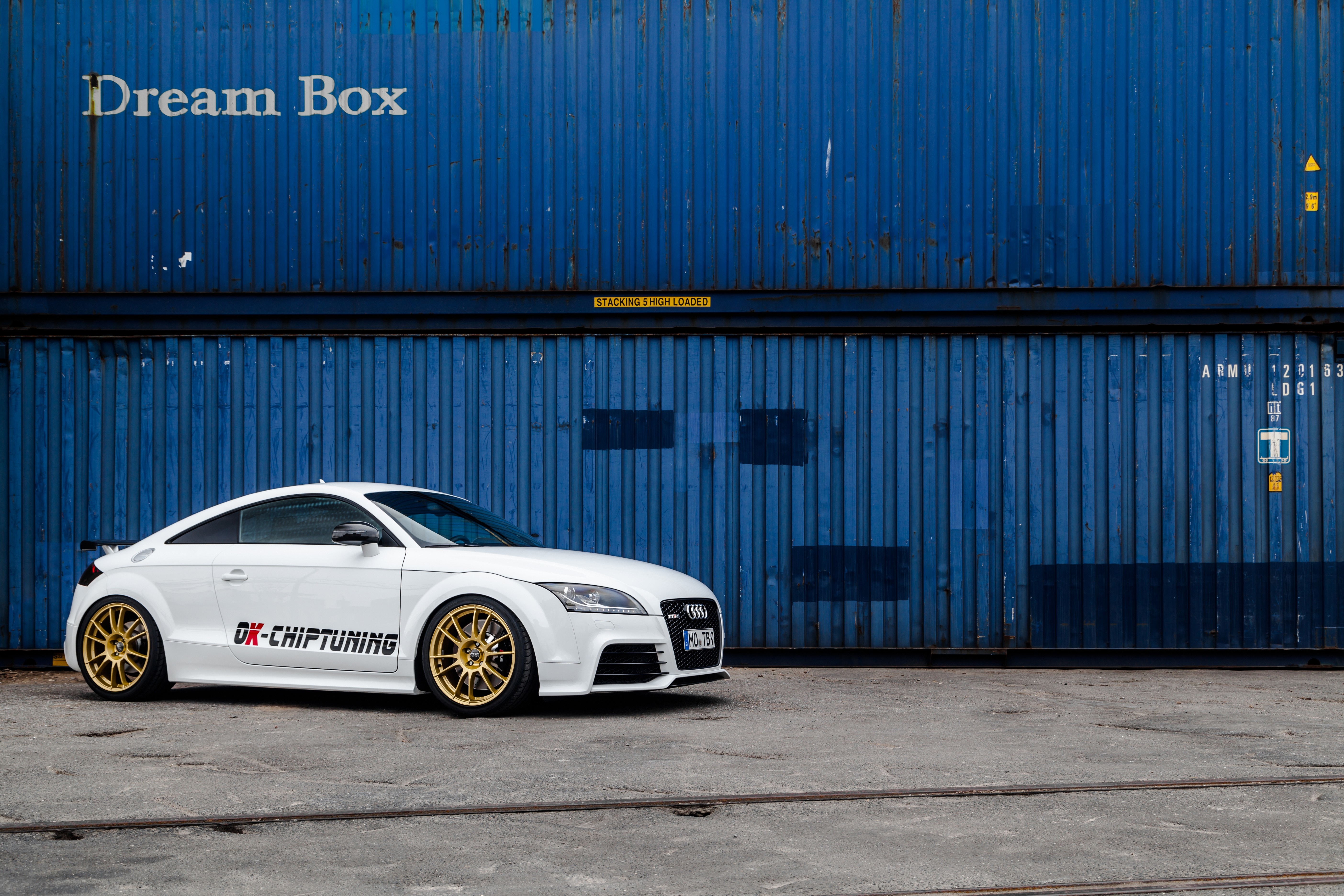 White Audi TT with gold wheels parked by blue shipping containers HD Wallpaper