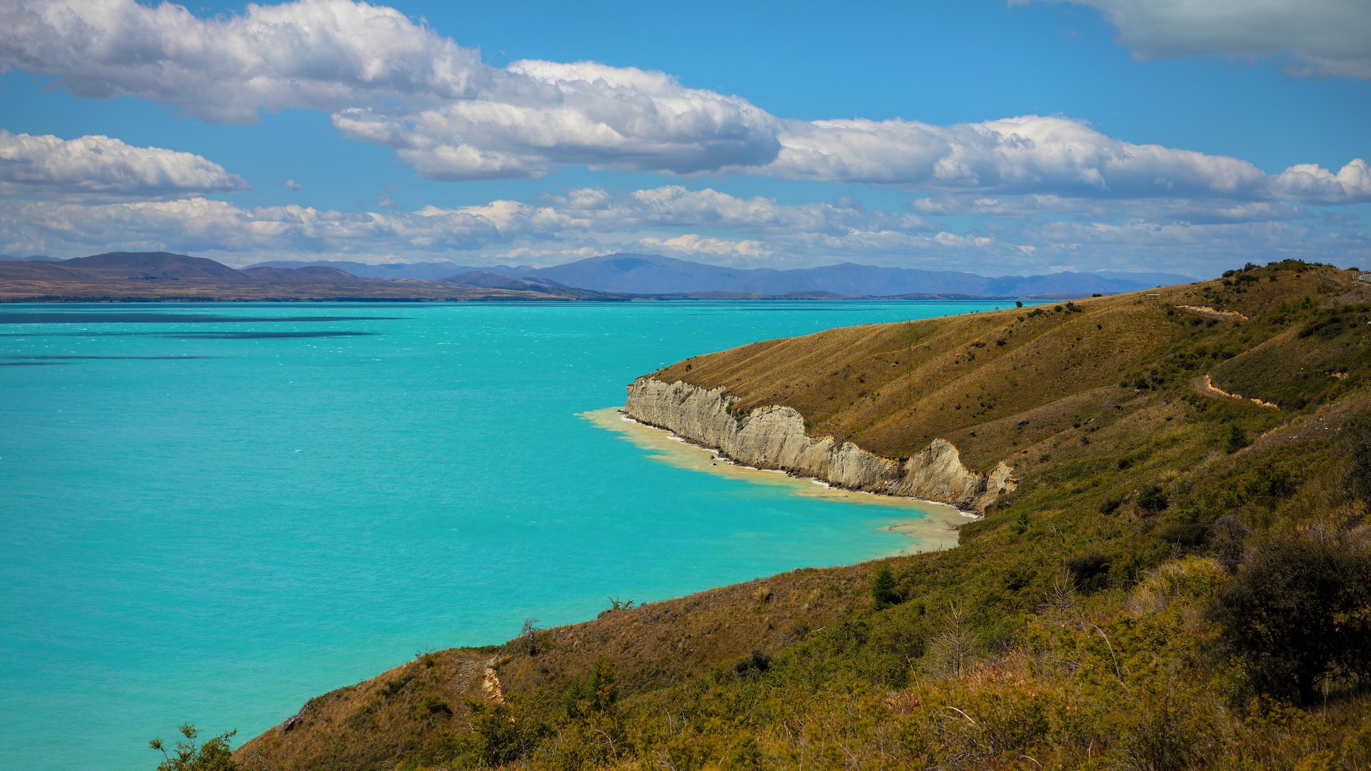 Turquoise lake and rolling hills under a blue sky HD Wallpaper