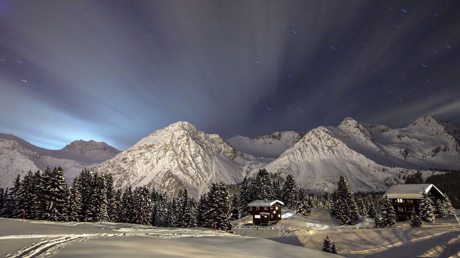 Snowy mountains at night with houses and trees HD Wallpaper