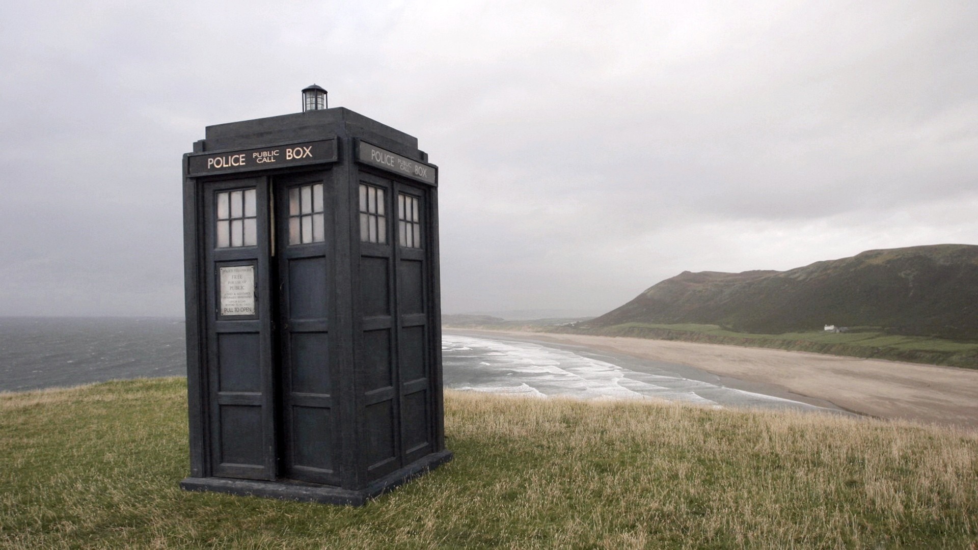 TARDIS Police Box on a grassy cliff overlooking a beach HD Wallpaper