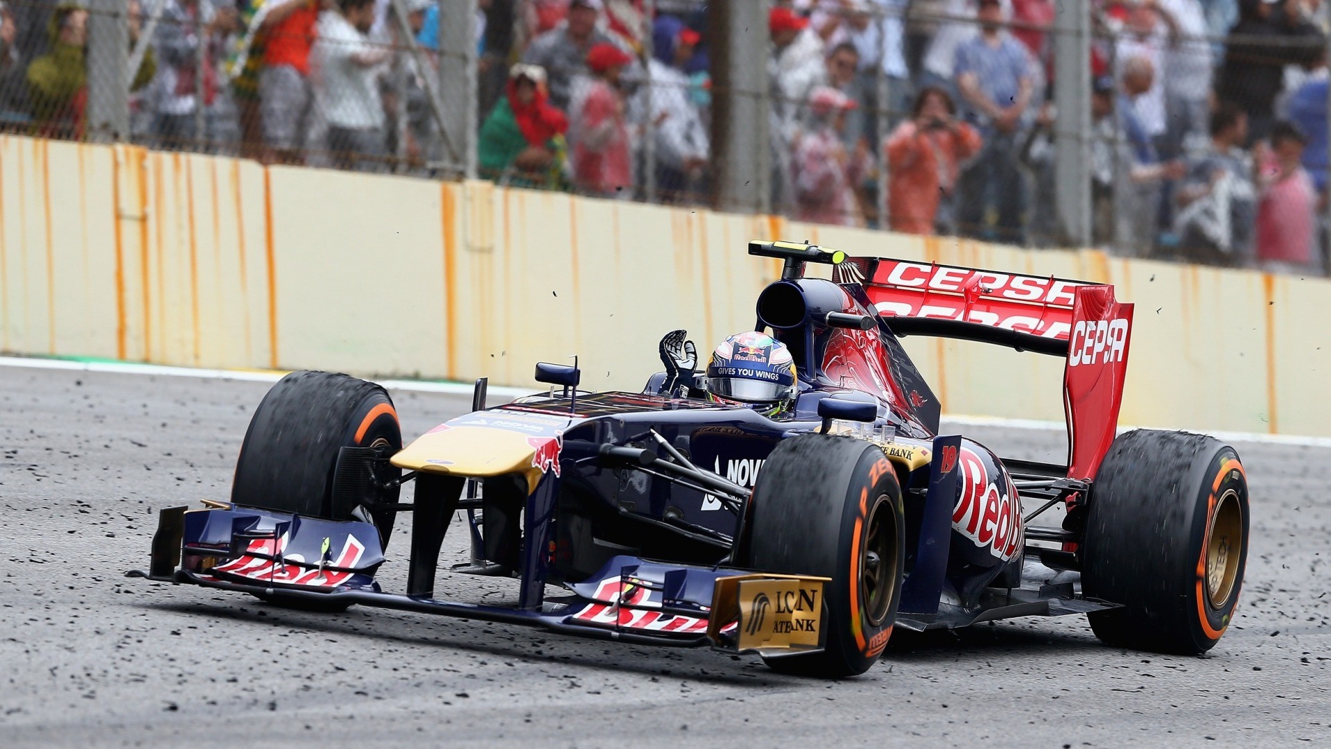 Formula 1 car racing on a track with spectators HD Wallpaper