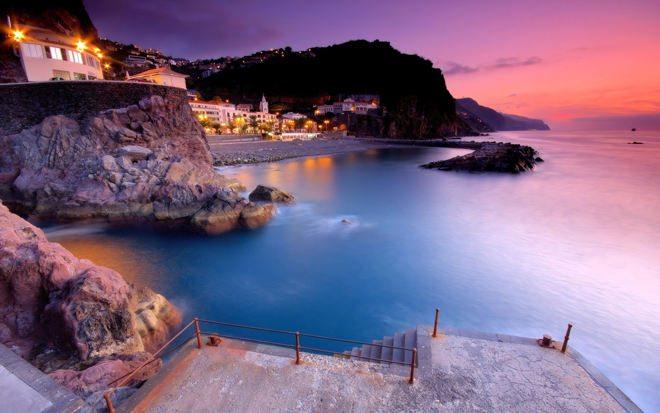 Coastal town at dusk with ocean and rocky shore HD Wallpaper