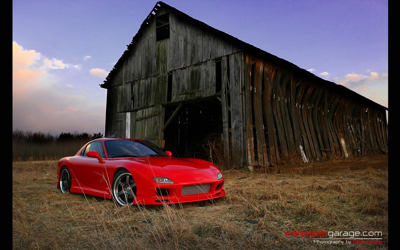 Red Mazda RX-7 parked by a weathered barn HD Wallpaper