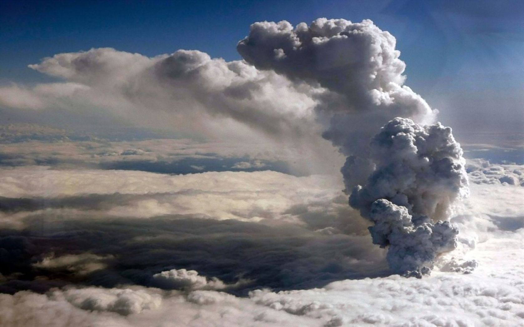 Volcanic ash cloud erupting into the sky above clouds HD Wallpaper