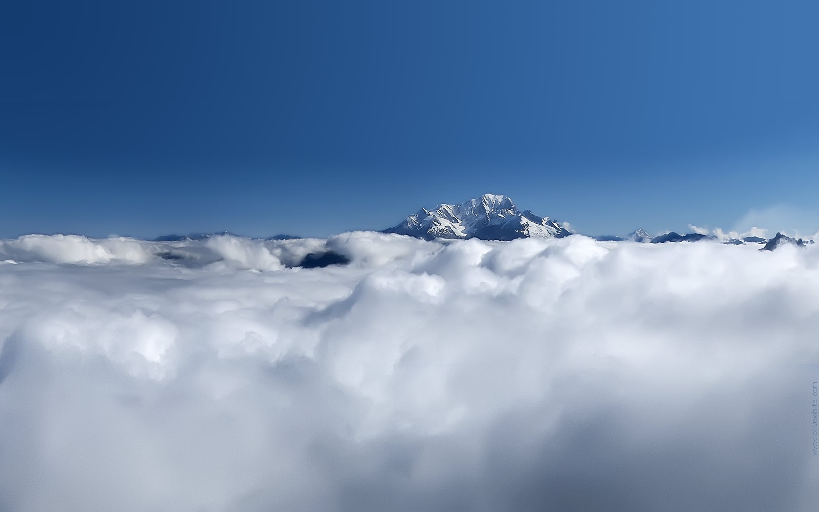 Snow-capped mountains above clouds under a blue sky HD Wallpaper