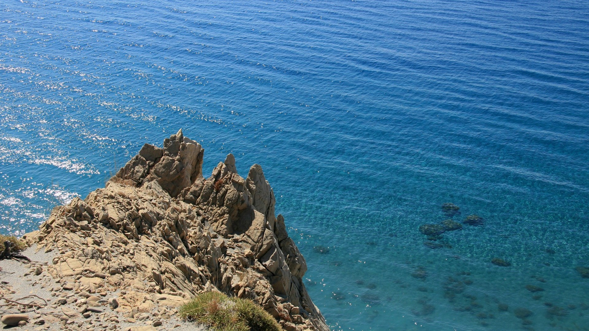 Rocky cliff overlooking a clear blue sea HD Wallpaper