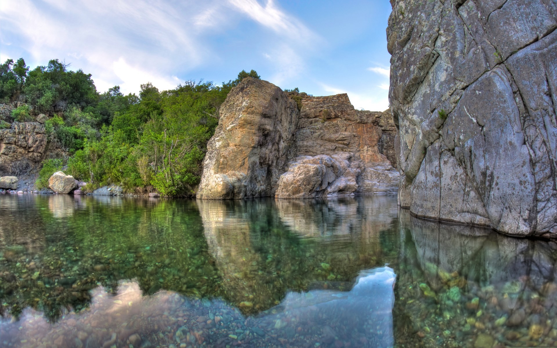 Clear river flowing between rocky cliffs and green trees HD Wallpaper